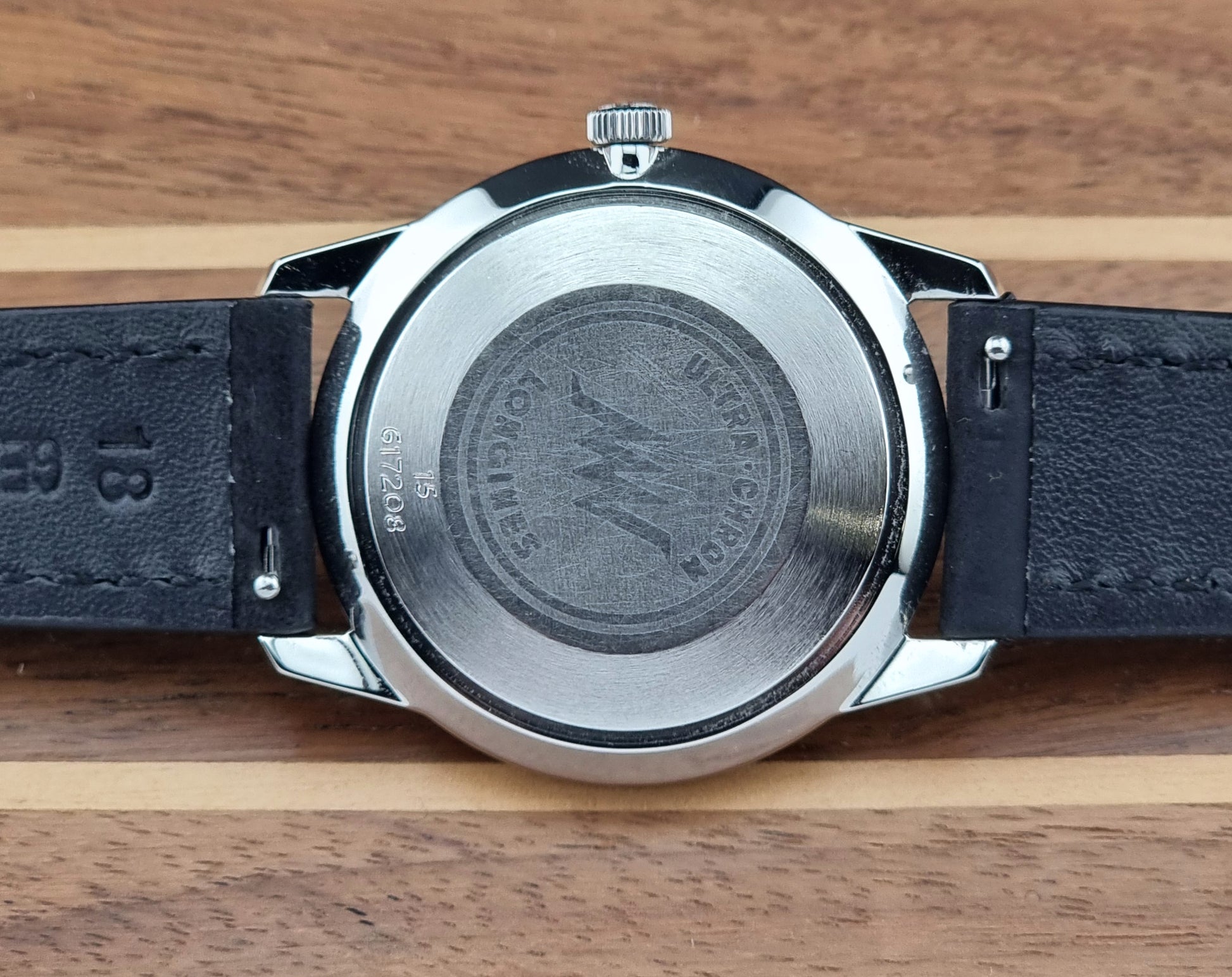 Back view of a watch with a black leather strap on a wooden surface