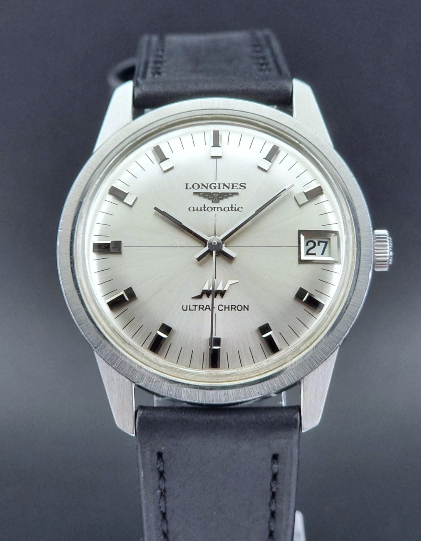 Longines watch with silver dial and black leather strap on a dark background