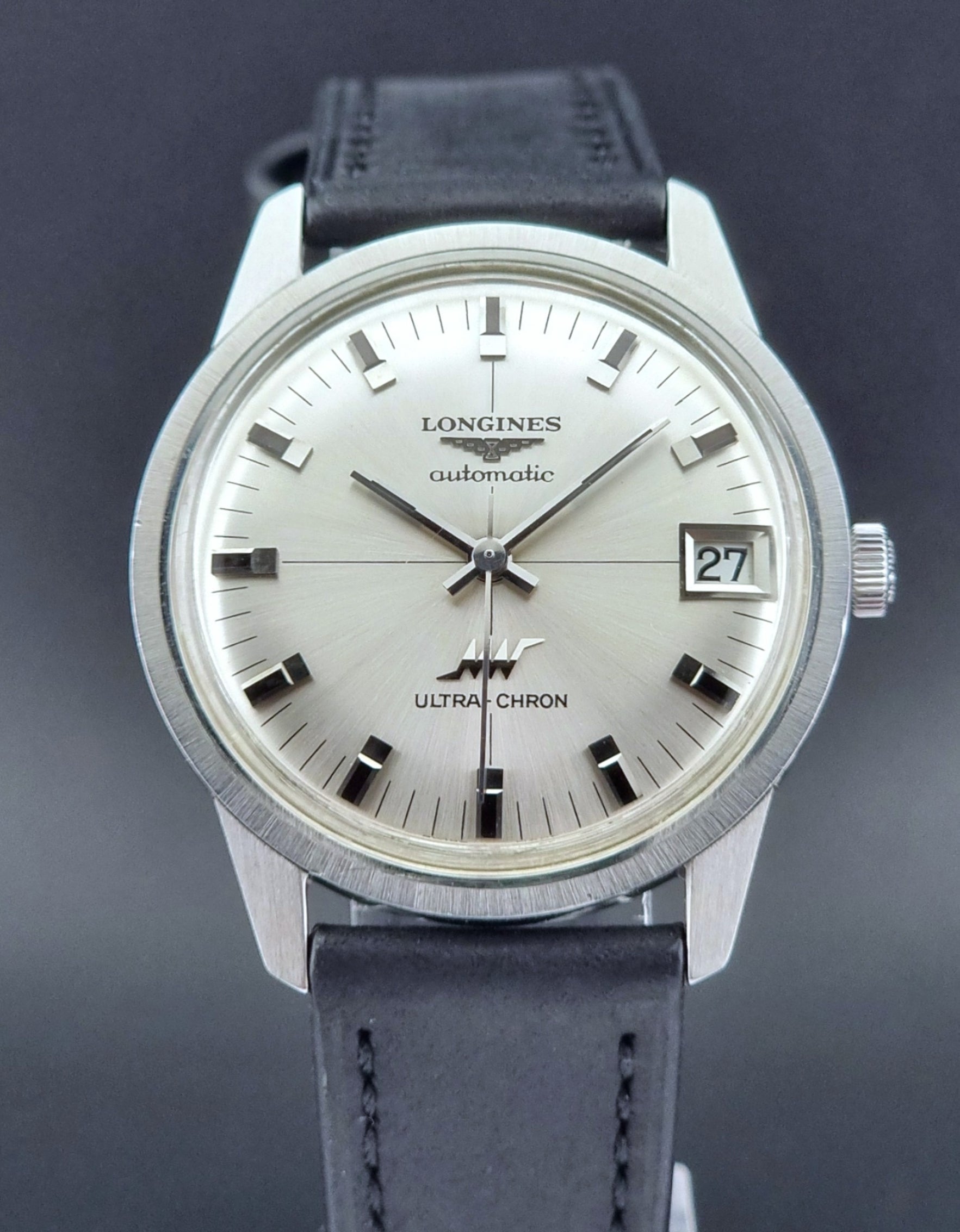 Longines watch with silver dial and black leather strap on a dark background