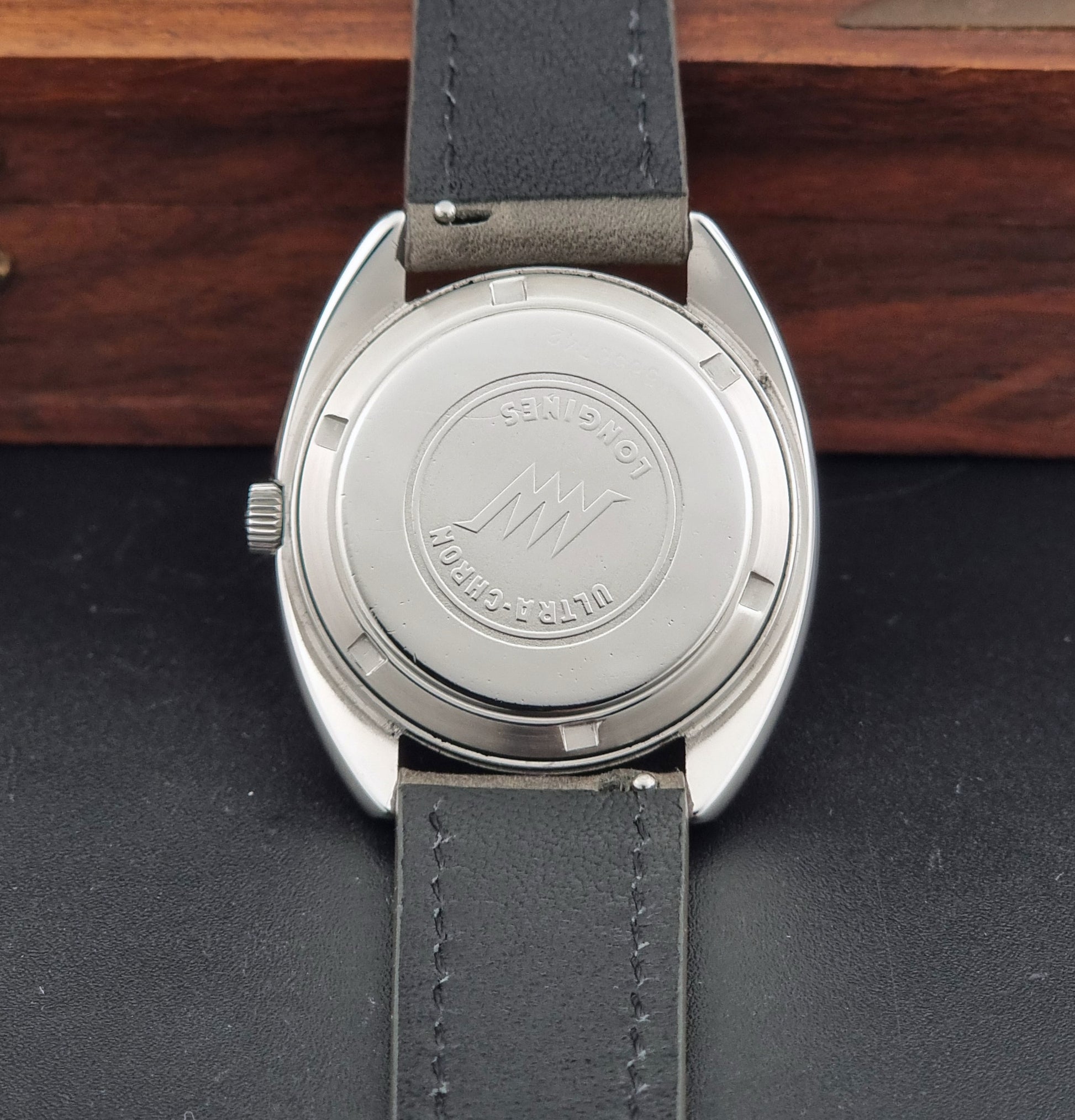 Vintage Longines ULTRA-CHRON 8353-1 watch with gray leather strap and silver case on a dark background case back view