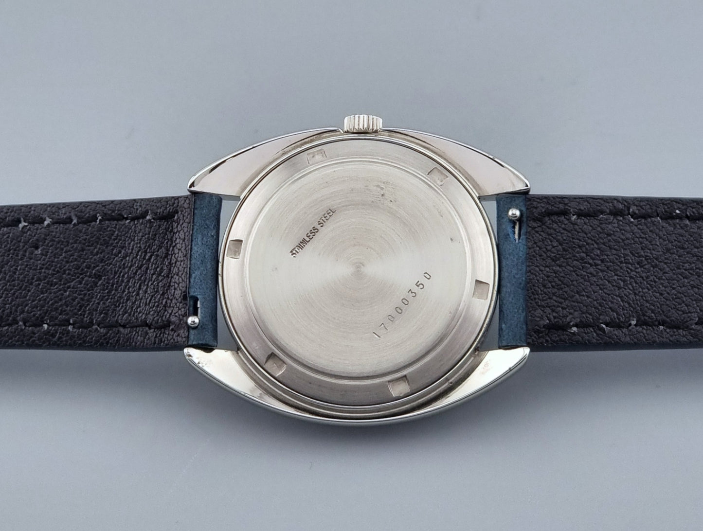Vintage Longines Ultra-Chron wristwatch  case back with blue strap and silver case on a gray background