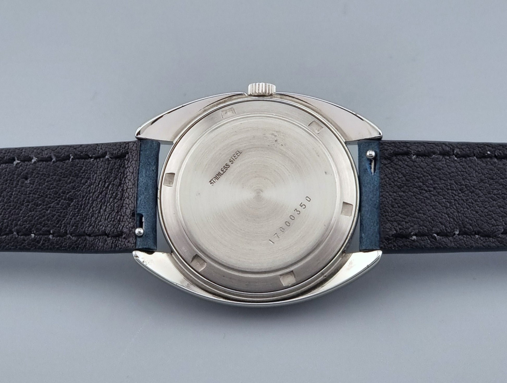 Vintage Longines Ultra-Chron wristwatch  case back with blue strap and silver case on a gray background