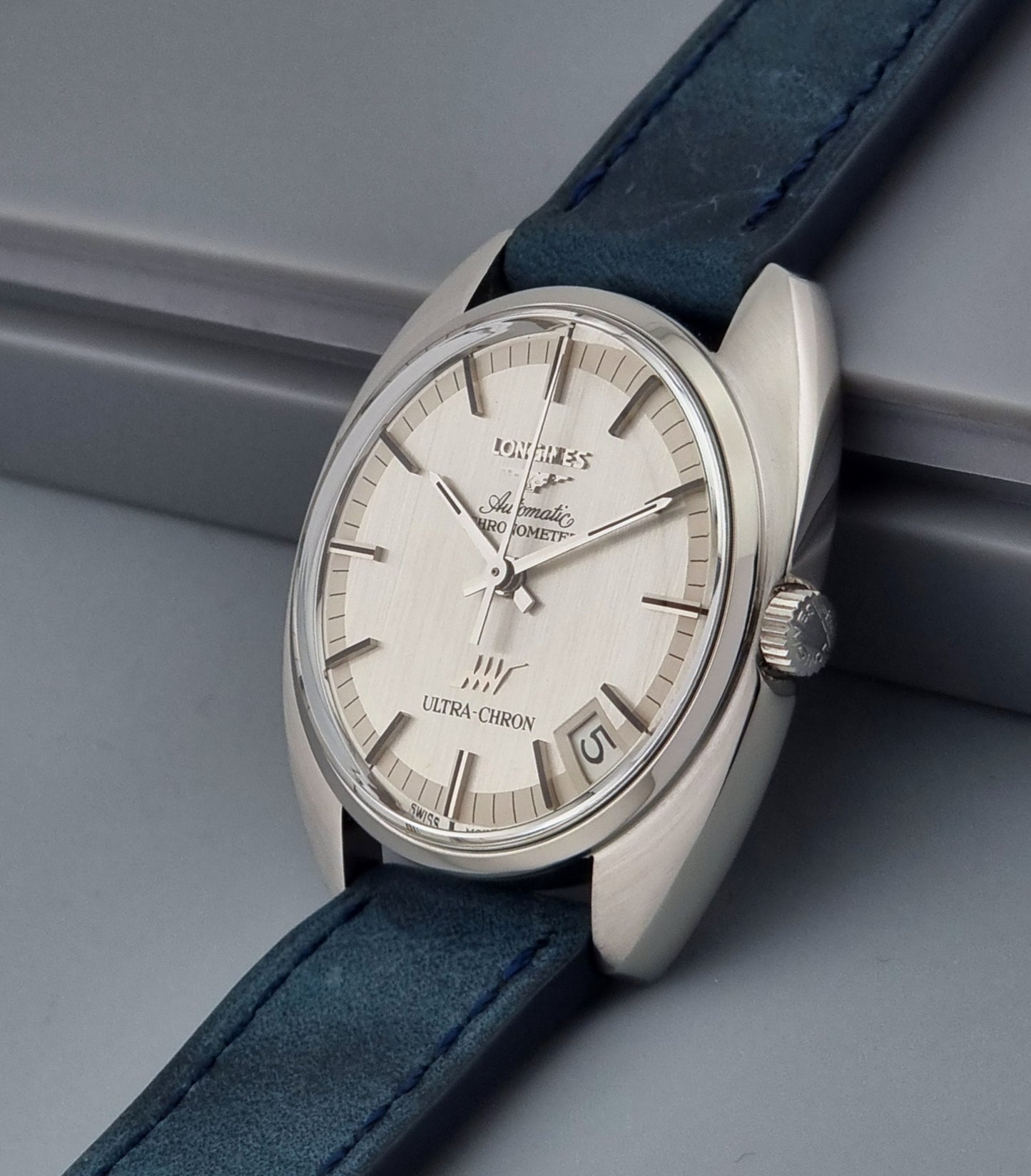 Vintage Longines Ultra-Chron wristwatch with blue strap and silver case on a gray background