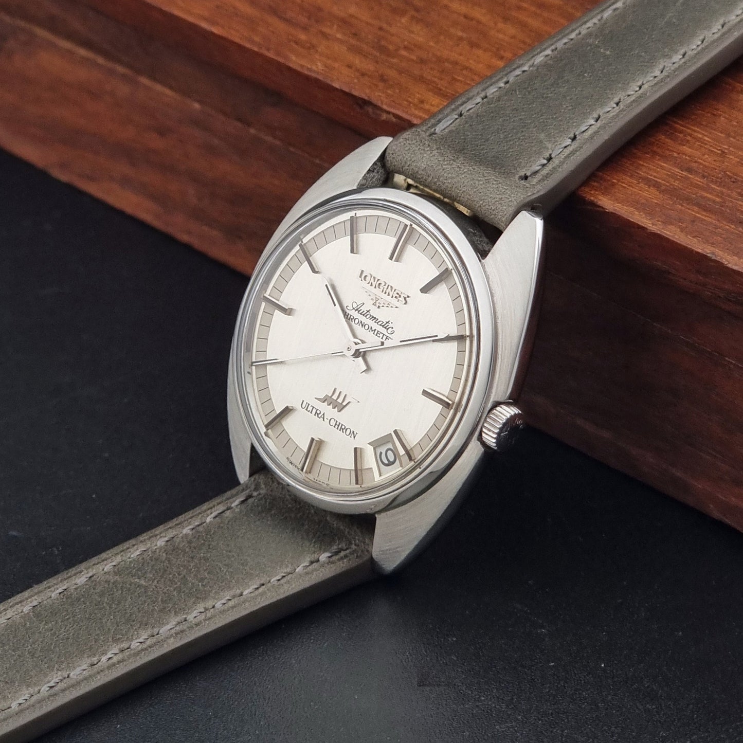 Vintage Longines ULTRA-CHRON 8353-1 watch with gray leather strap and silver case on a dark background crown view