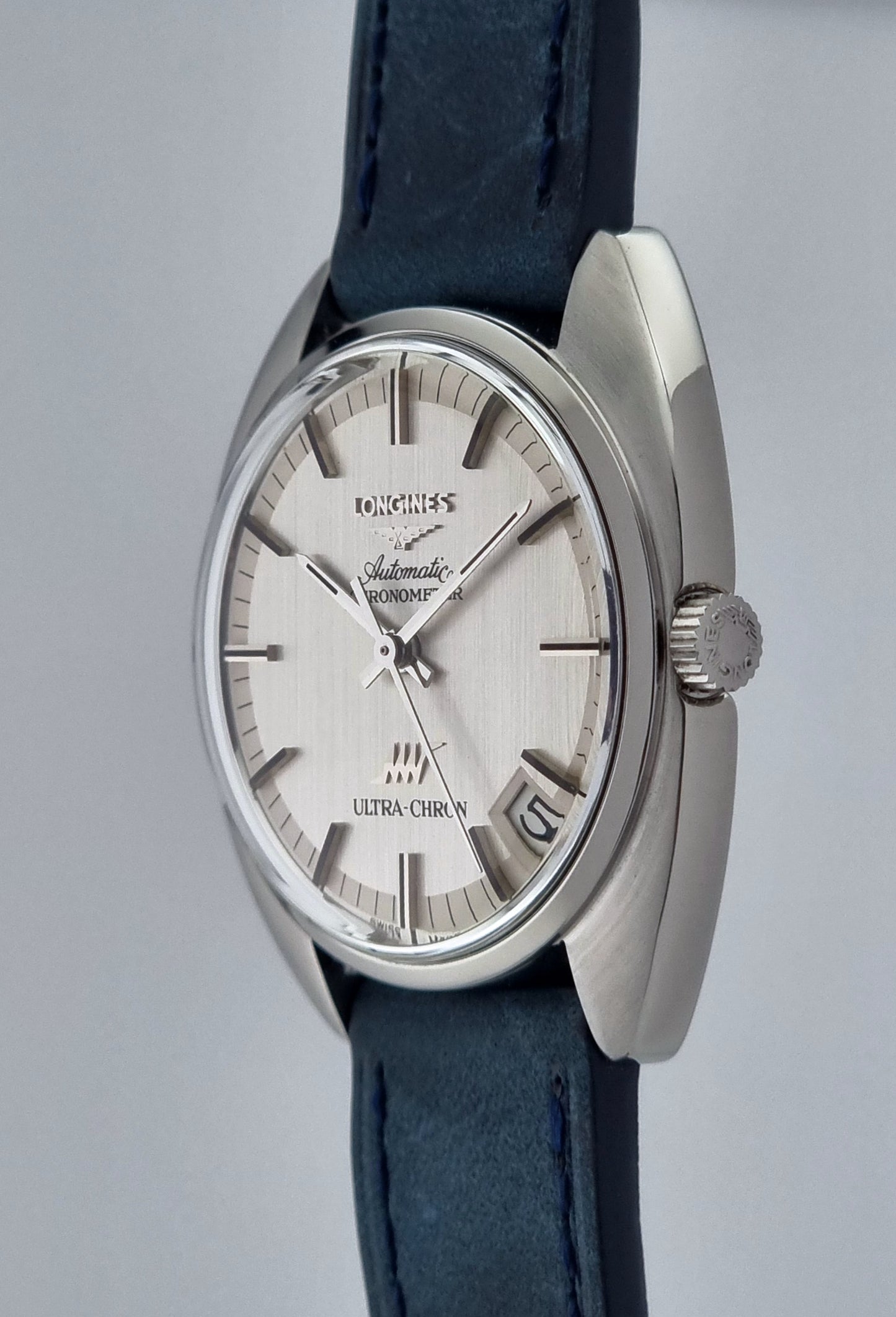 Vintage Longines Ultra-Chron wristwatch with blue strap and silver case on a gray background