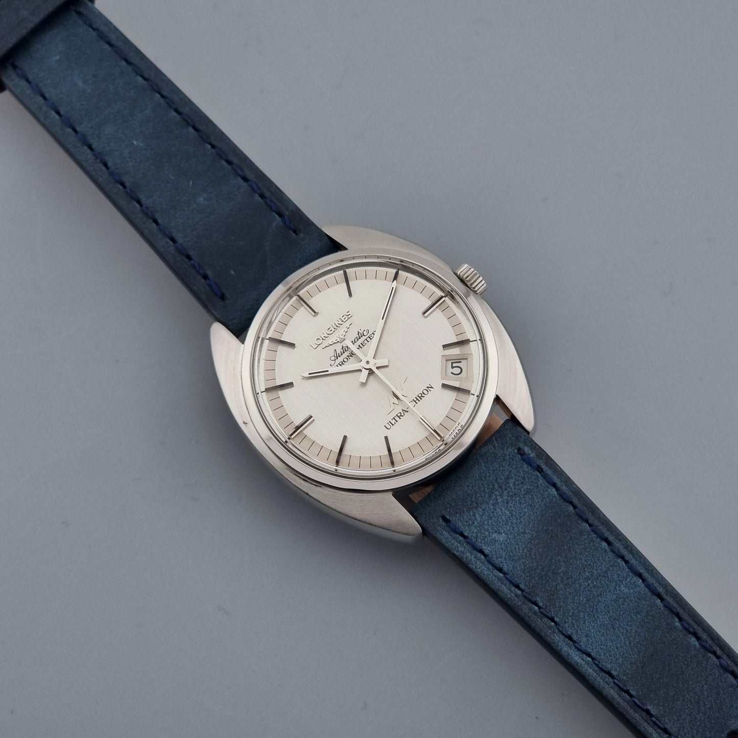 Vintage Longines Ultra-Chron wristwatch with blue strap and silver case on a gray background