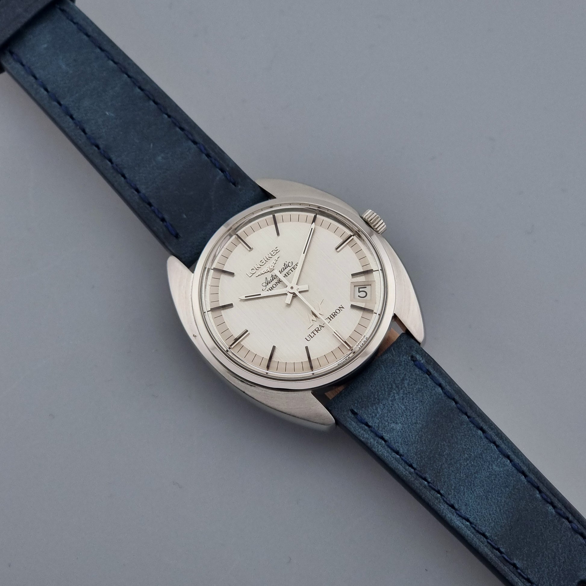 Vintage Longines Ultra-Chron wristwatch with blue strap and silver case on a gray background