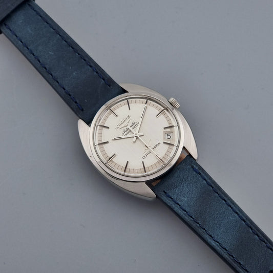 Vintage Longines Ultra-Chron wristwatch with blue strap and silver case on a gray background