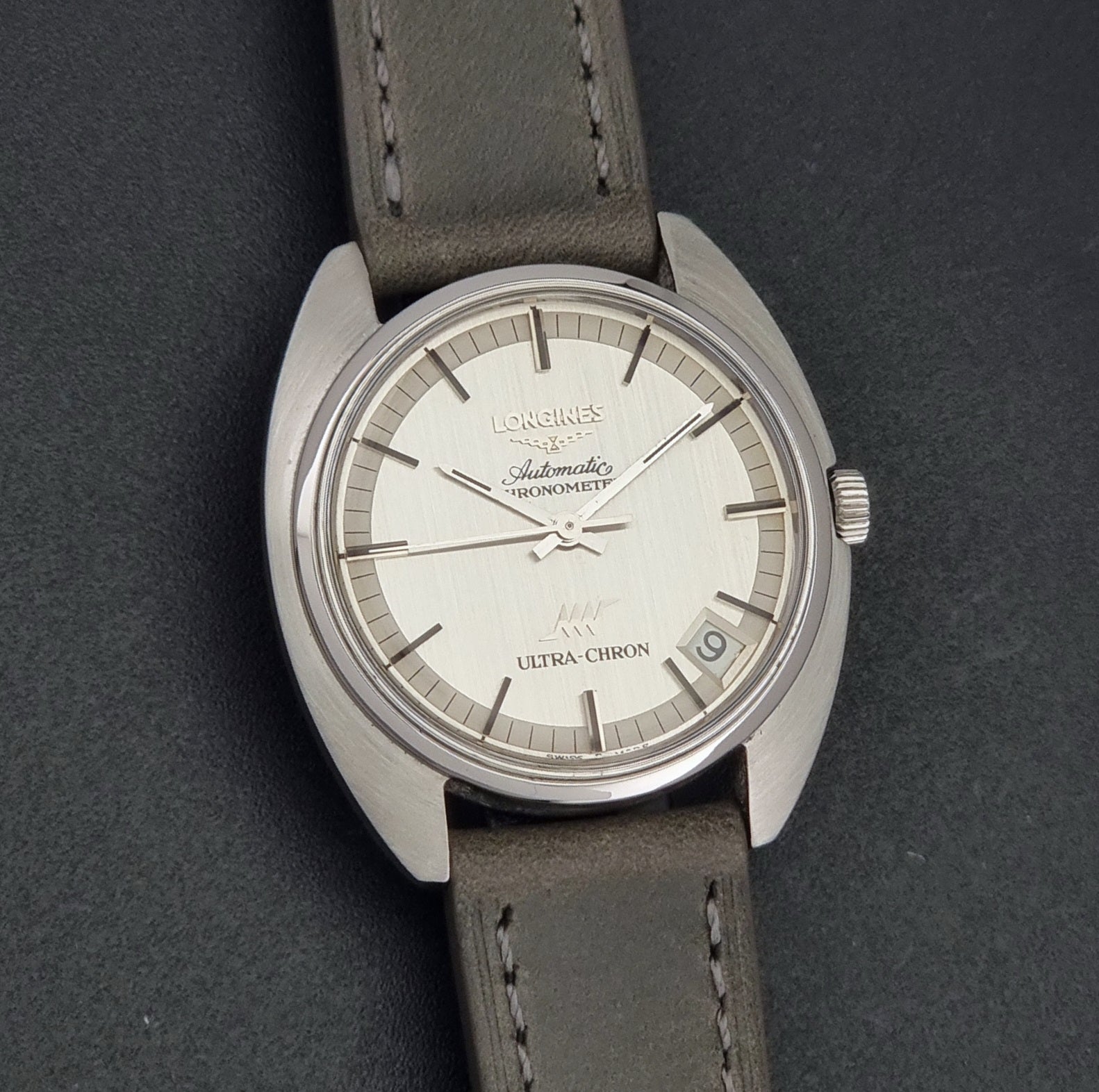 Vintage Longines ULTRA-CHRON 8353-1 watch with gray leather strap and silver case on a dark background front view