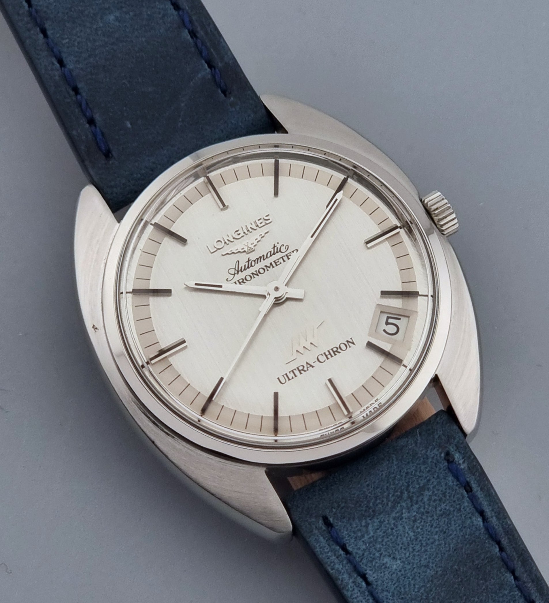 Vintage Longines Ultra-Chron wristwatch with blue strap and silver case on a gray background