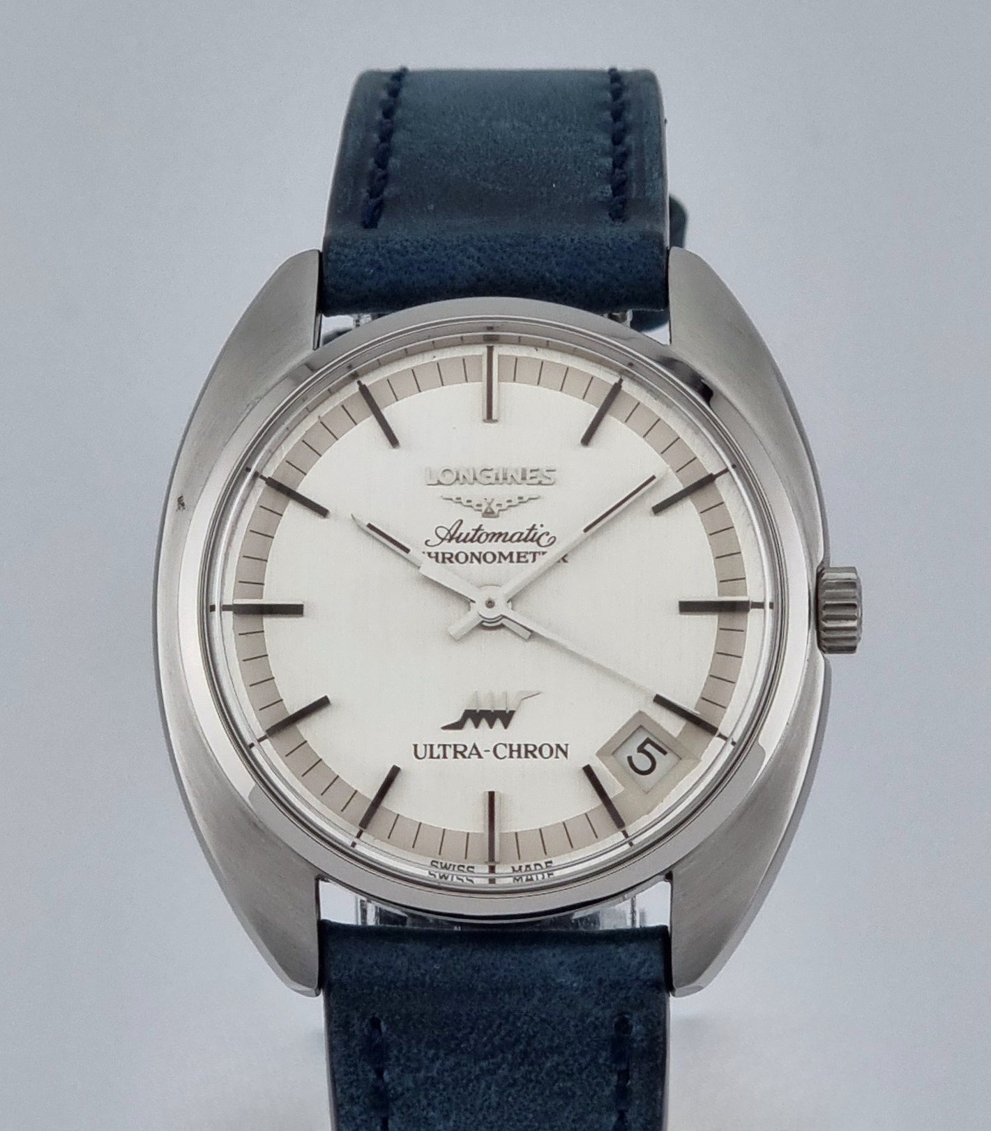 Vintage Longines Ultra-Chron wristwatch with blue strap and silver case on a grey background