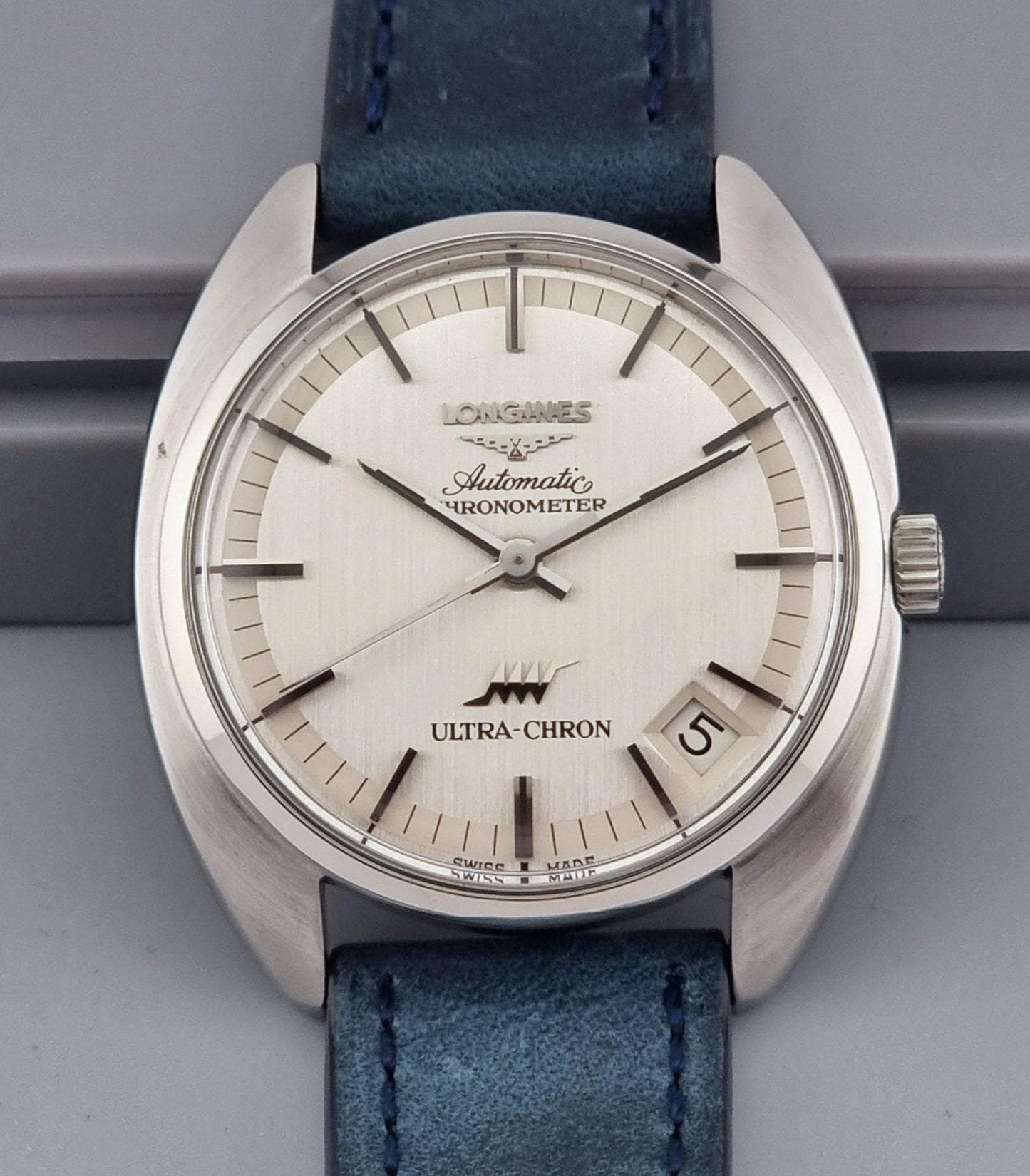 Vintage Longines Ultra-Chron wristwatch with blue strap and silver case on a gray background
