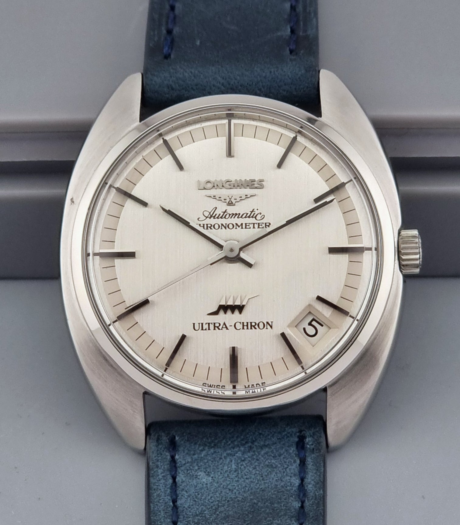 Vintage Longines Ultra-Chron wristwatch with blue strap and silver case on a gray background