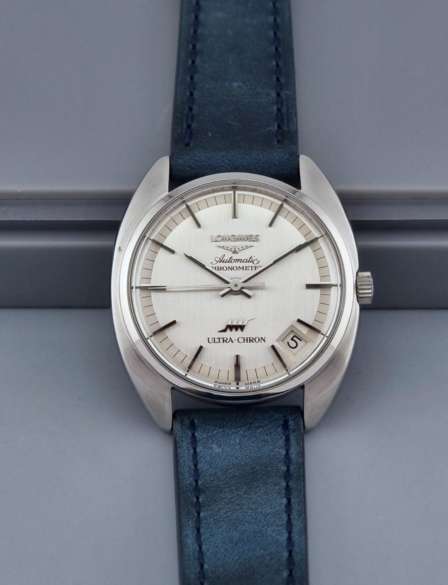 Vintage Longines Ultra-Chron wristwatch with blue strap and silver case on a gray background