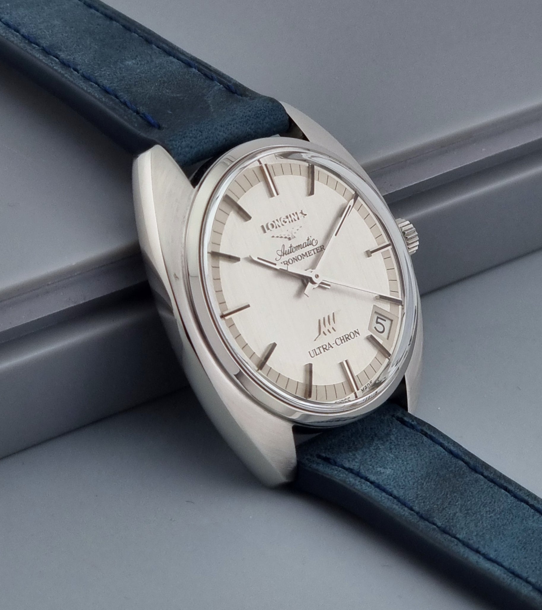Vintage Longines Ultra-Chron wristwatch with blue strap and silver case on a gray background