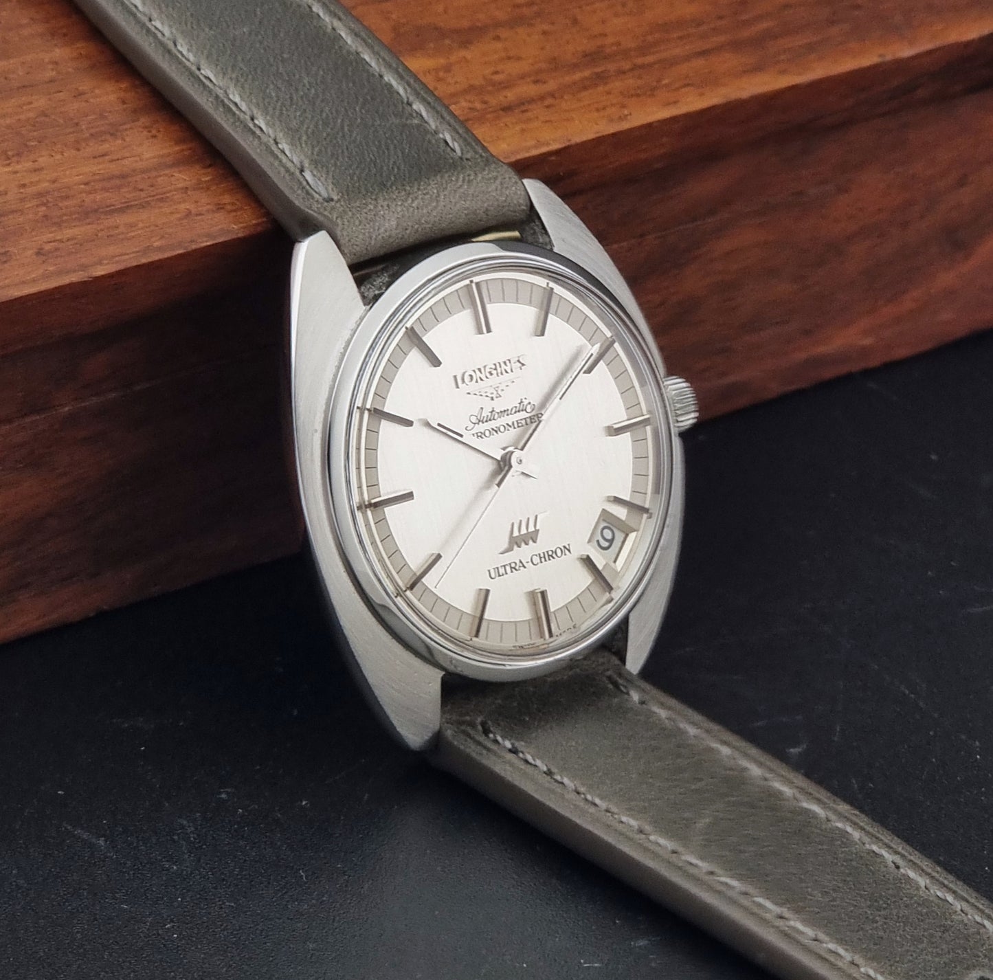 Vintage Longines ULTRA-CHRON 8353-1 watch with gray leather strap and silver case on a dark background side view