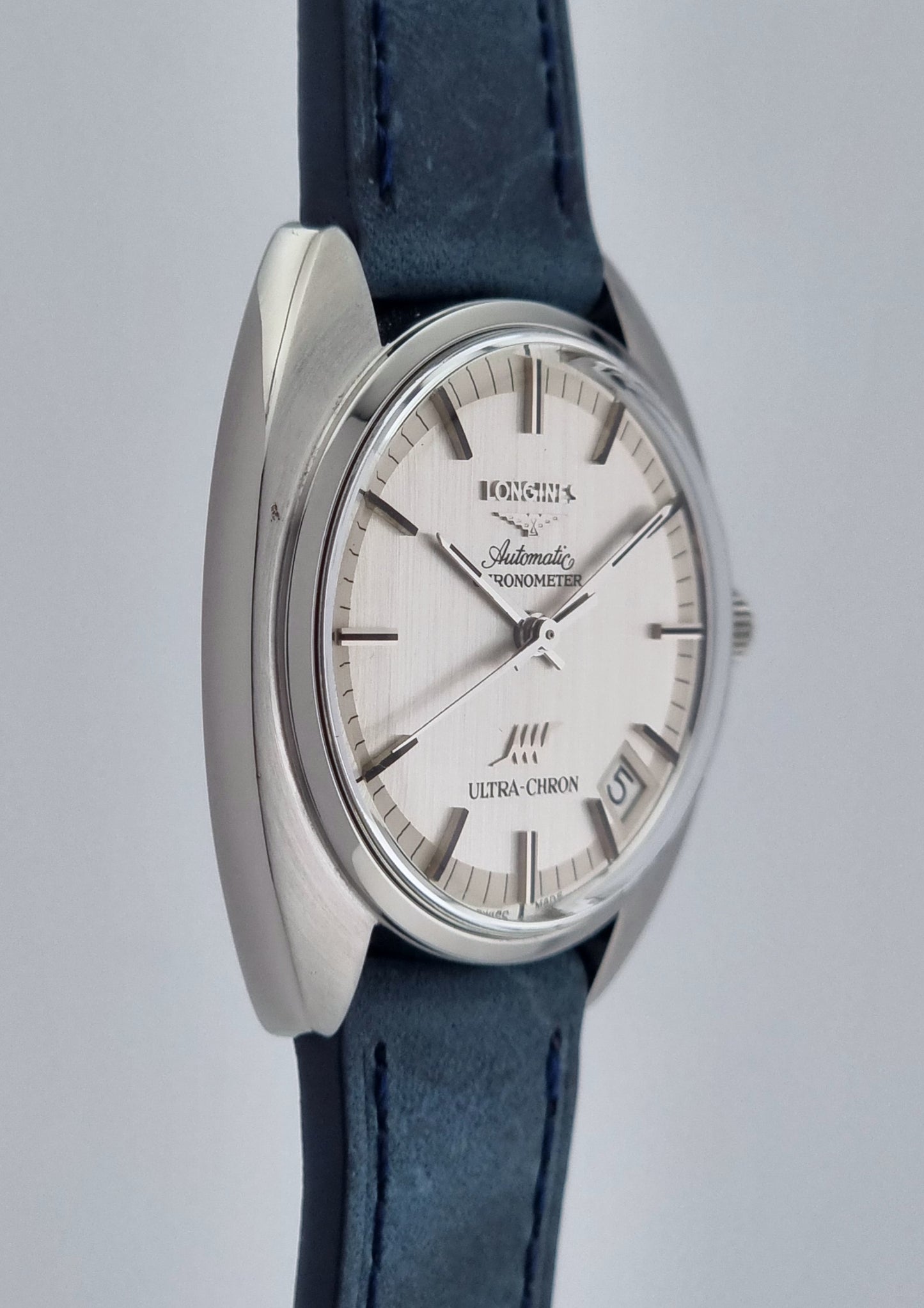Vintage Longines Ultra-Chron wristwatch with blue strap and silver case on a gray background