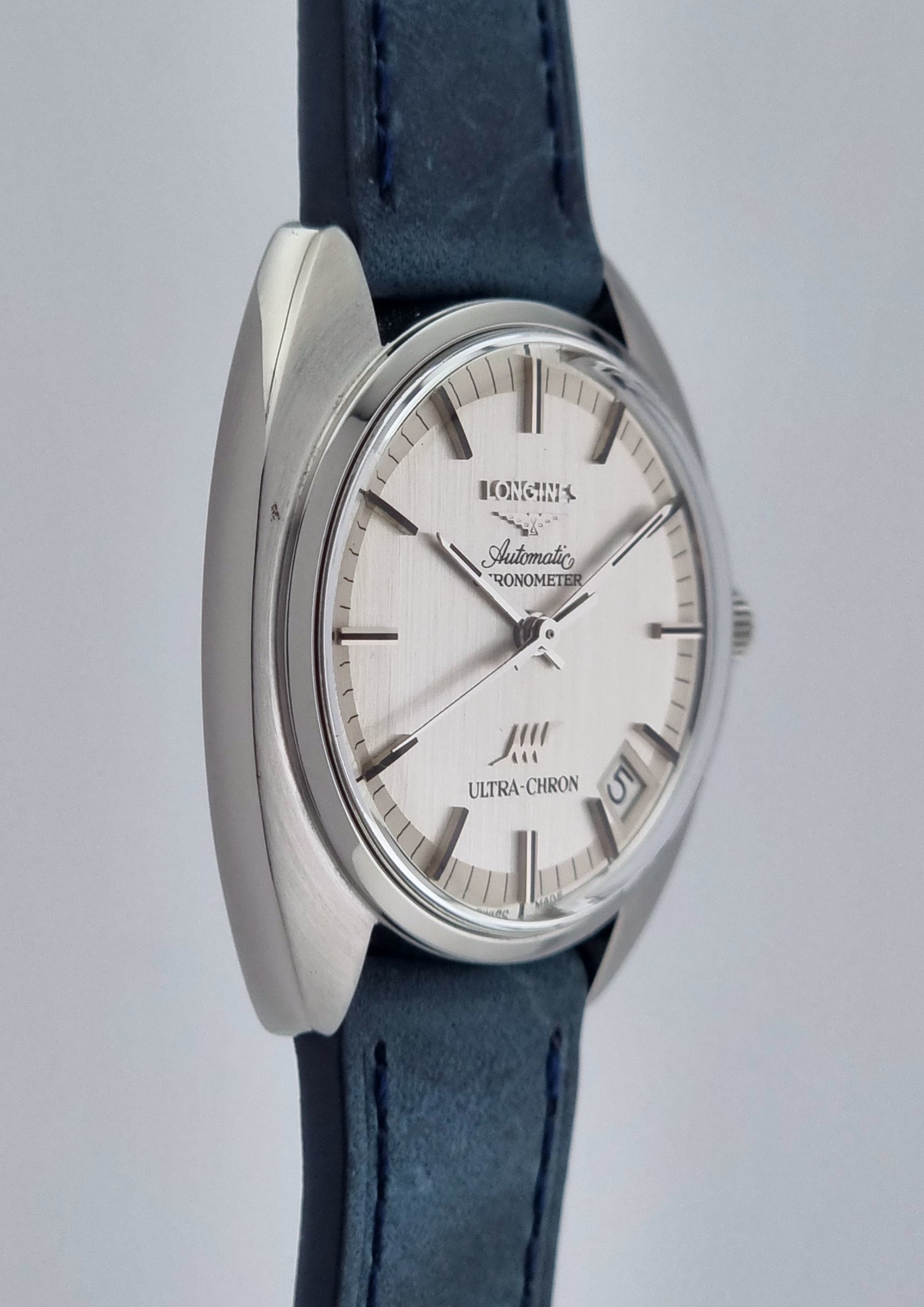 Vintage Longines Ultra-Chron wristwatch with blue strap and silver case on a gray background