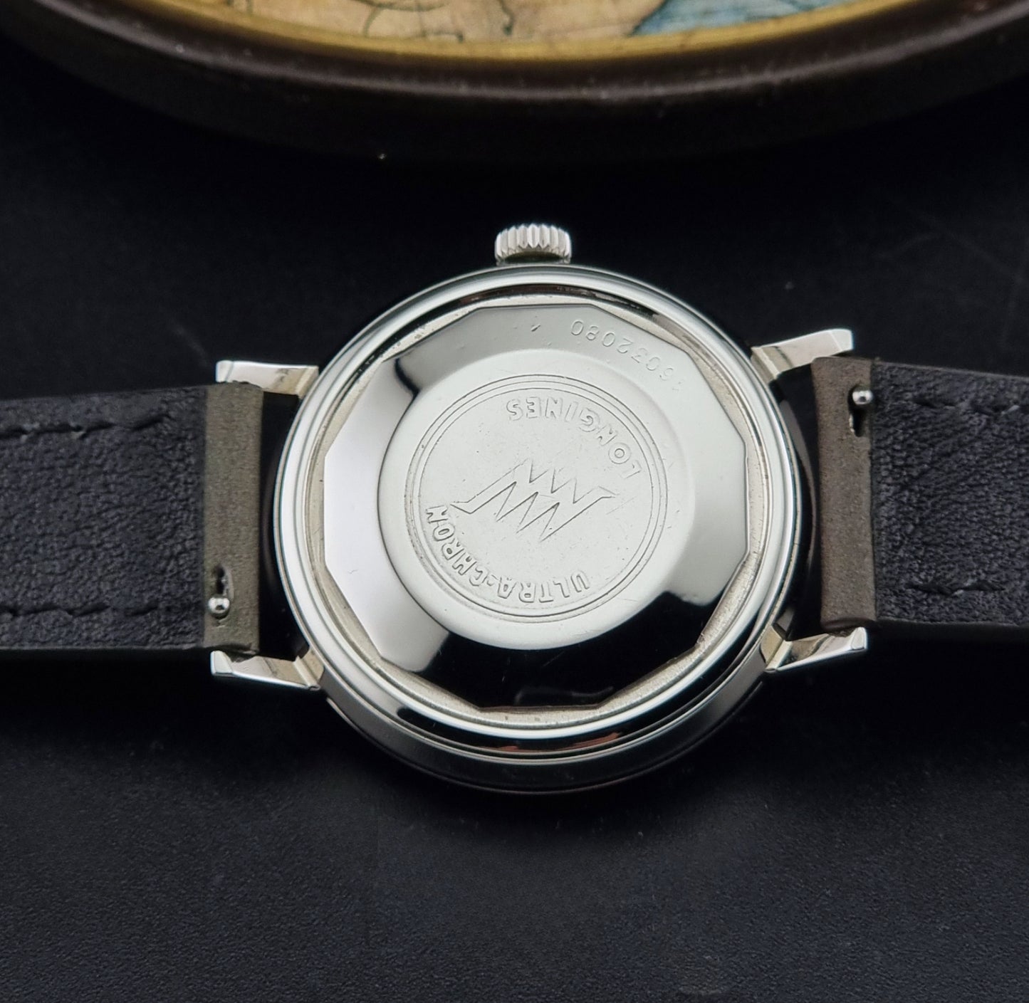 Vintage Longines ULTRA-CHRON 8383-1 watch with a silver-toned round case and gray leather strap on a dark gray background case back view