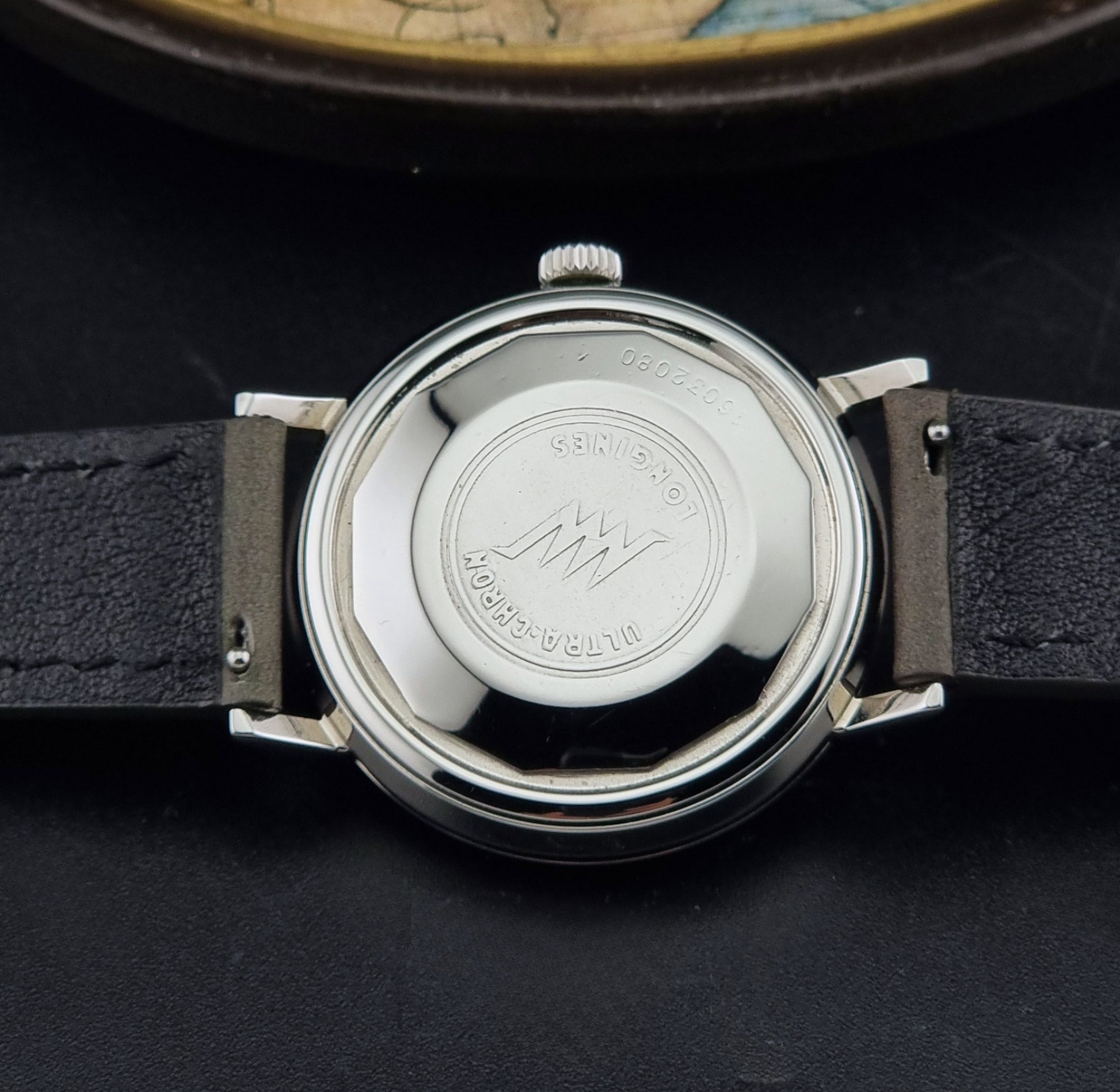 Vintage Longines ULTRA-CHRON 8383-1 watch with a silver-toned round case and gray leather strap on a dark gray background case back view