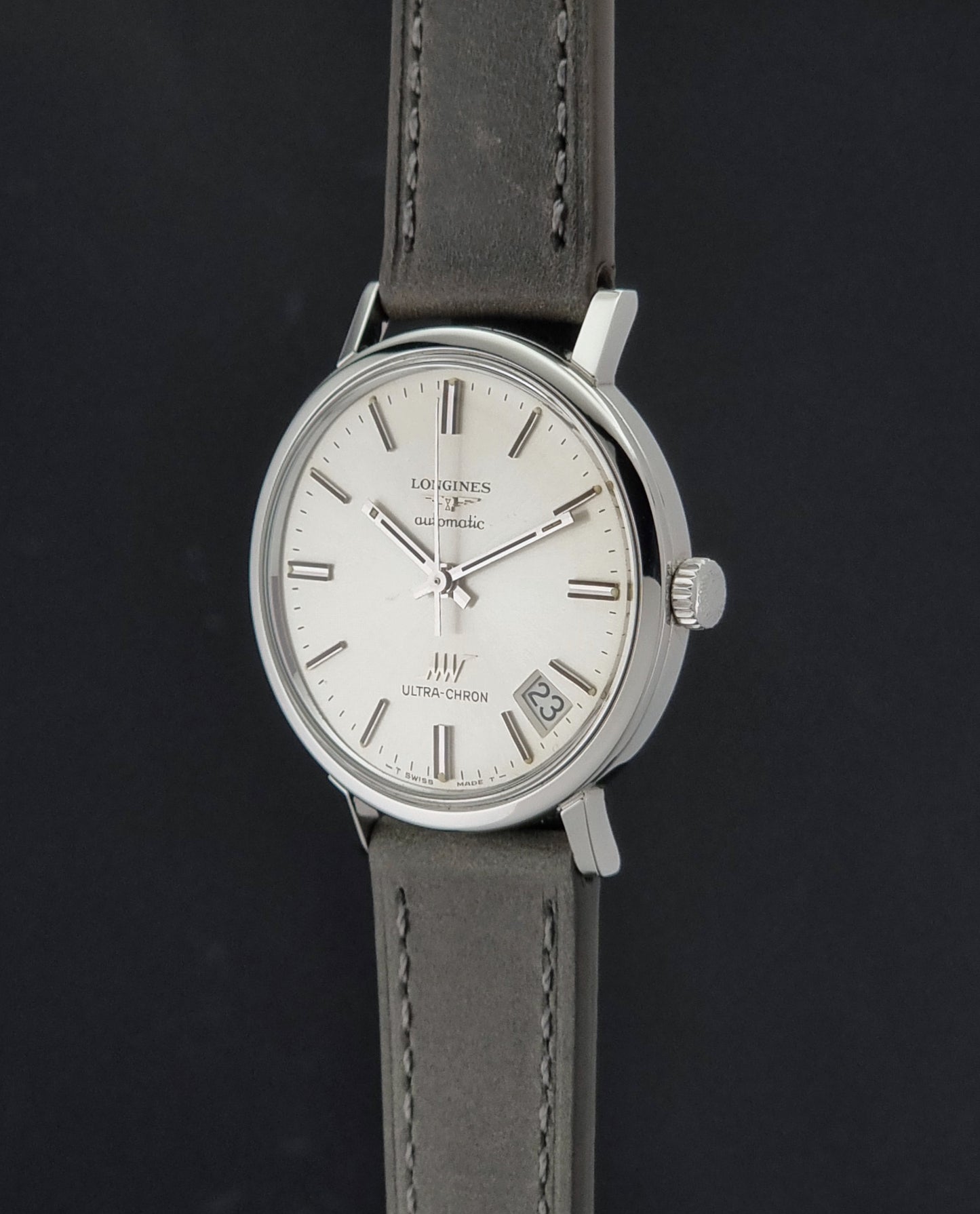 Vintage Longines ULTRA-CHRON 8383-1 watch with a silver-toned round case and gray leather strap on a dark gray background crown profile view