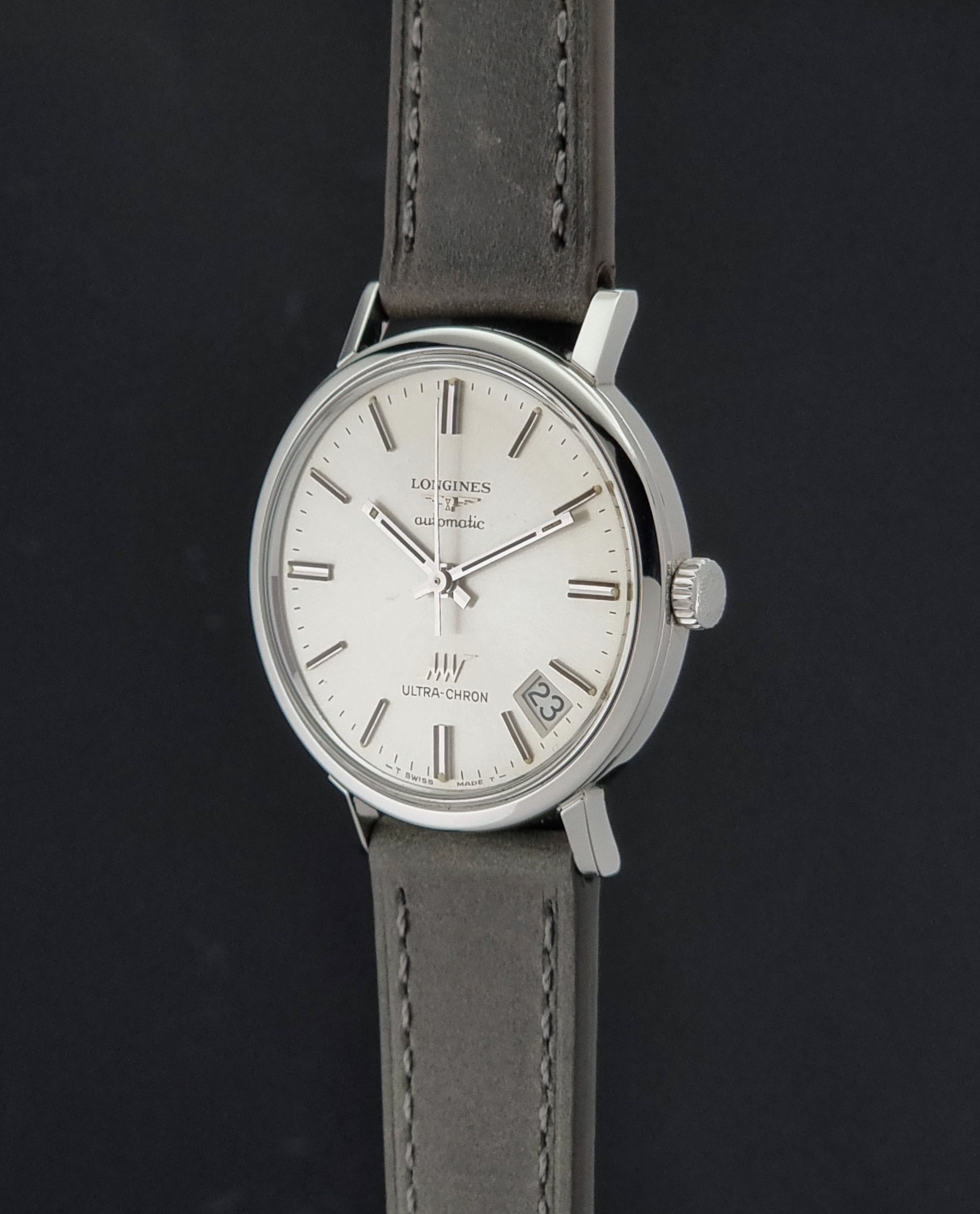 Vintage Longines ULTRA-CHRON 8383-1 watch with a silver-toned round case and gray leather strap on a dark gray background crown profile view