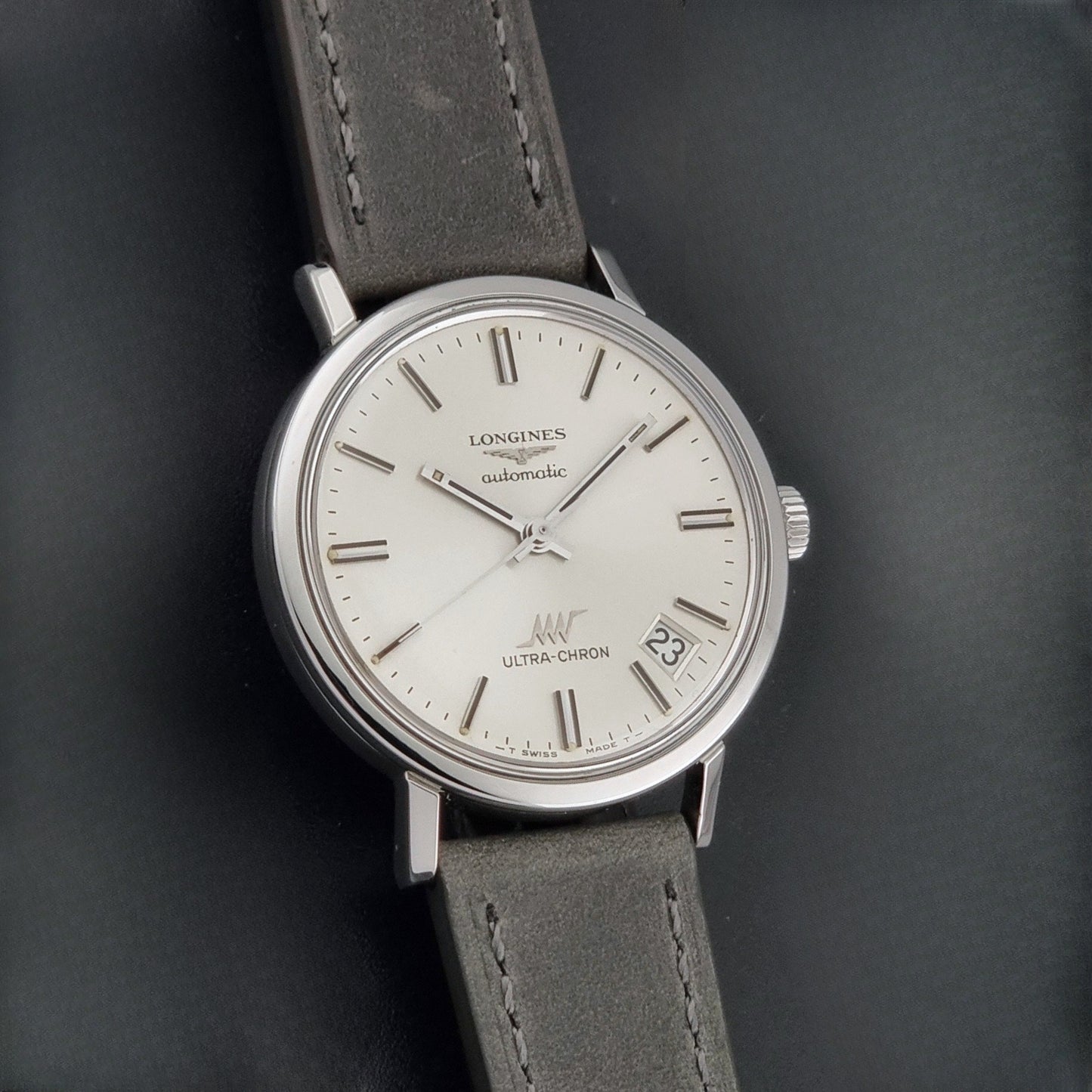 Vintage Longines ULTRA-CHRON 8383-1 watch with a silver-toned round case and gray leather strap on a dark gray background front view