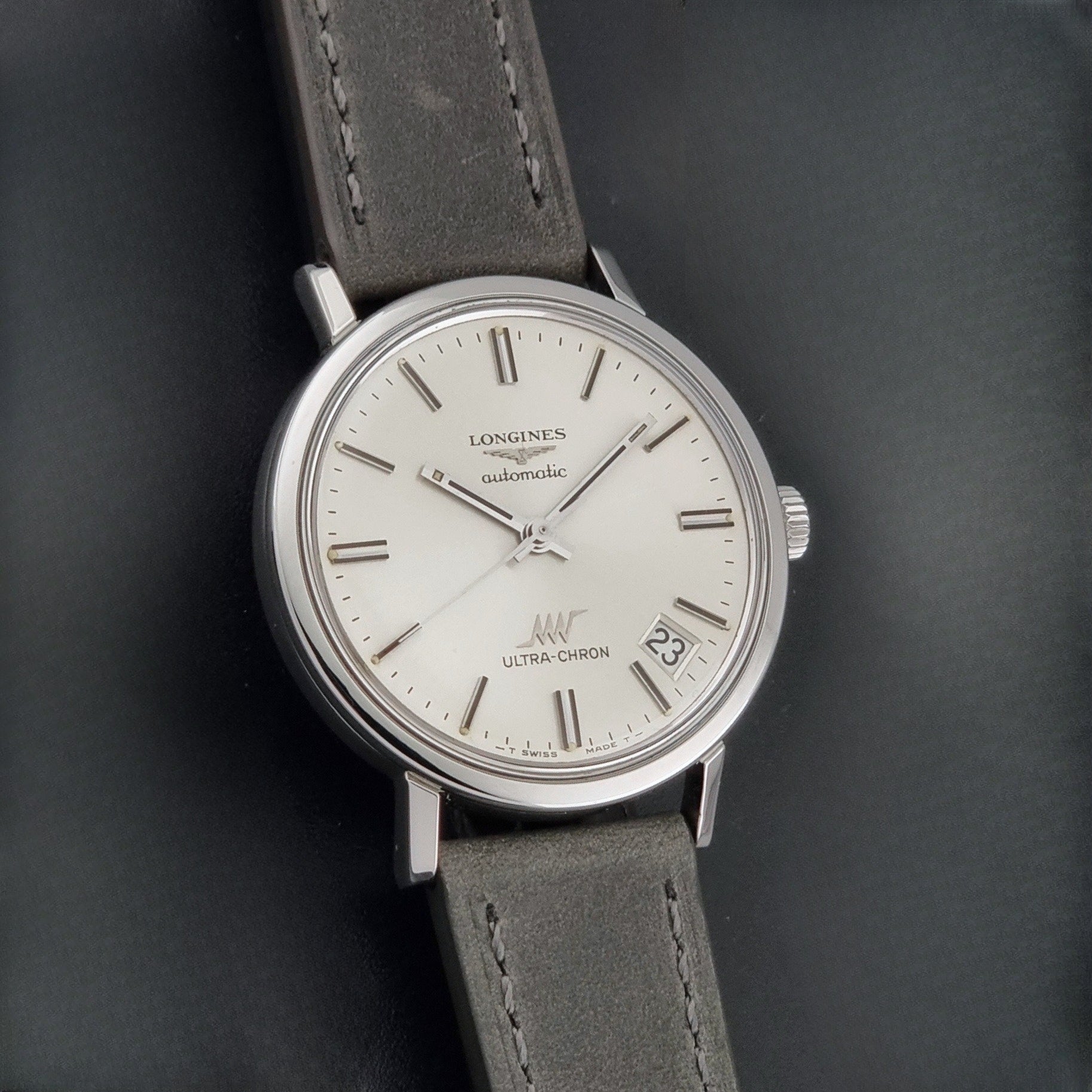 Vintage Longines ULTRA-CHRON 8383-1 watch with a silver-toned round case and gray leather strap on a dark gray background front view