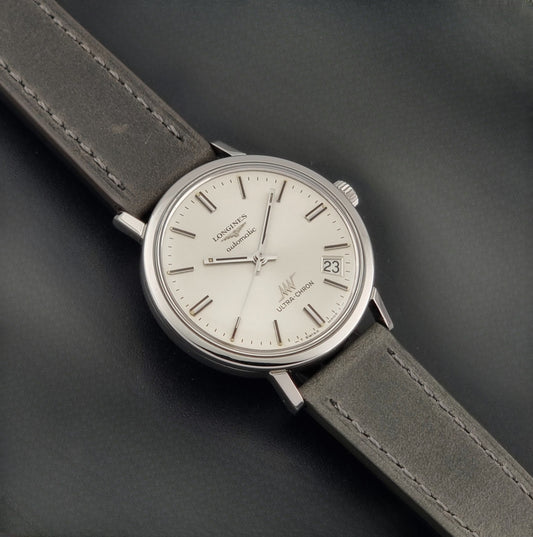 Vintage Longines ULTRA-CHRON 8383-1 watch with a silver-toned round case and gray leather strap on a dark gray background dial