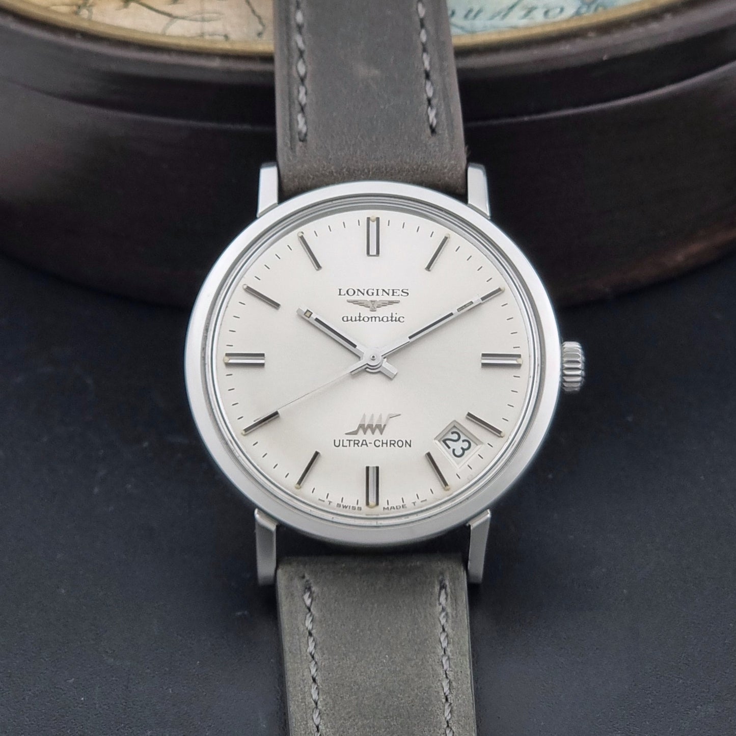 Vintage Longines ULTRA-CHRON 8383-1 watch with a silver-toned round case and gray leather strap on a dark gray background dial view