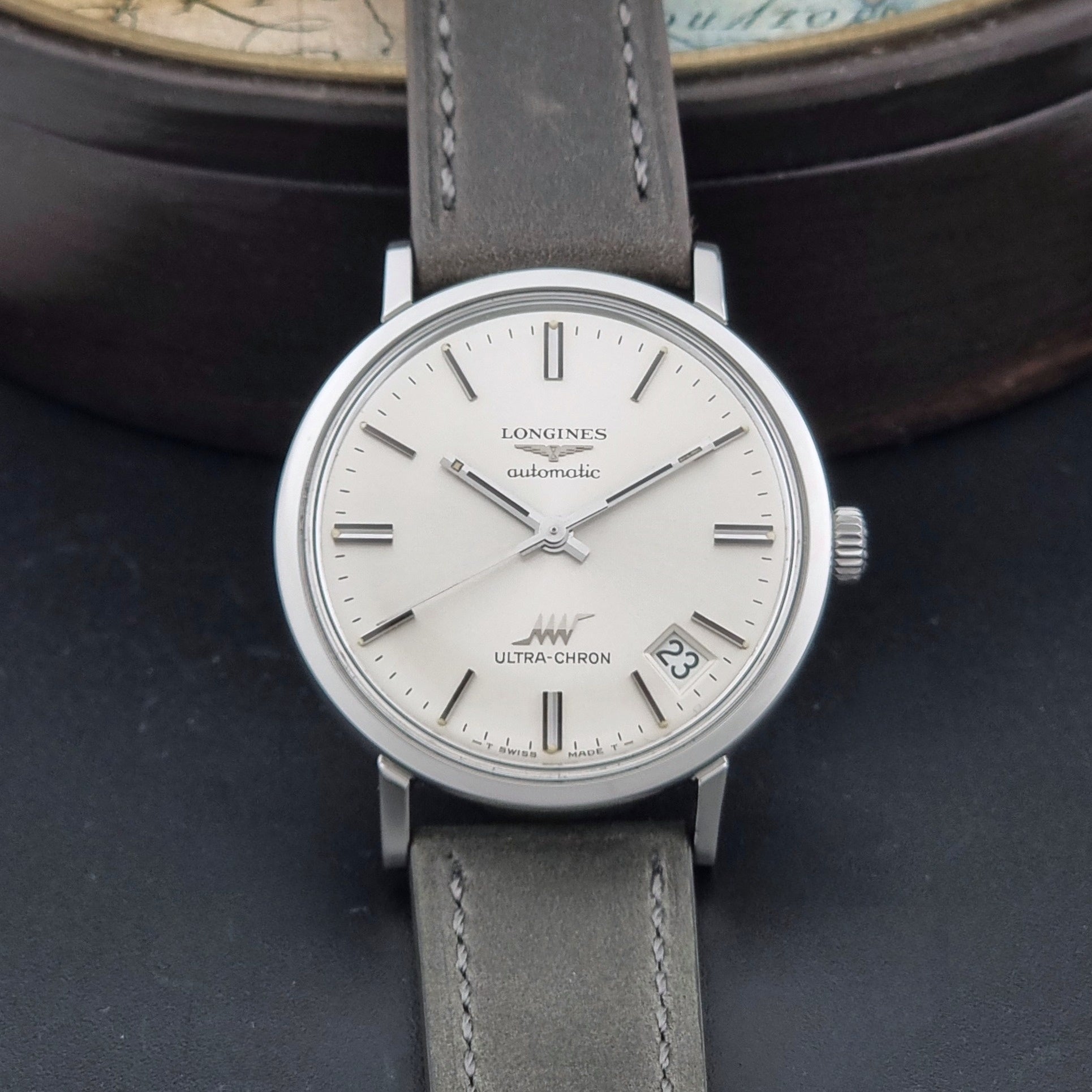 Vintage Longines ULTRA-CHRON 8383-1 watch with a silver-toned round case and gray leather strap on a dark gray background dial view