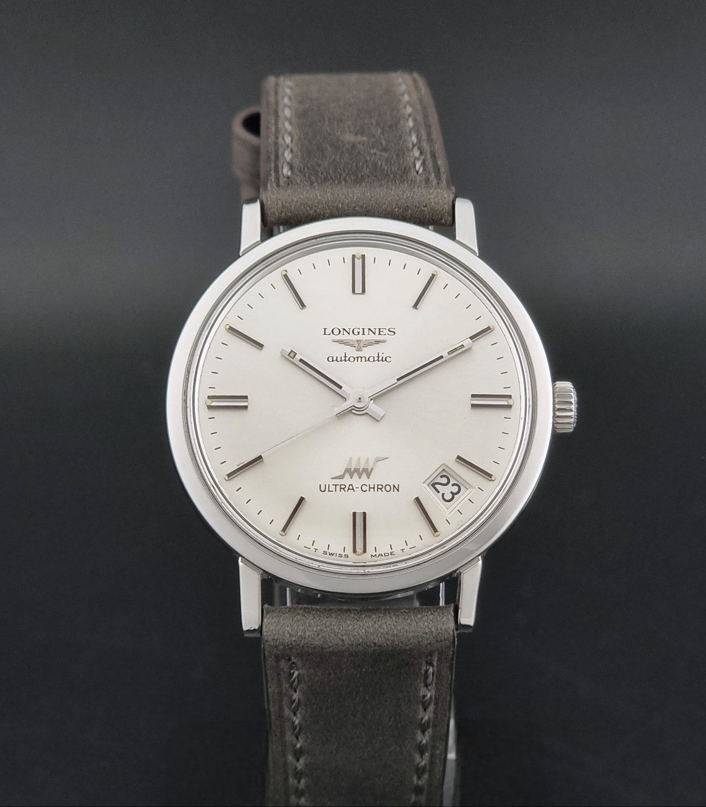 Vintage Longines ULTRA-CHRON 8383-1 watch with a silver-toned round case and gray leather strap on a dark gray background close dial view