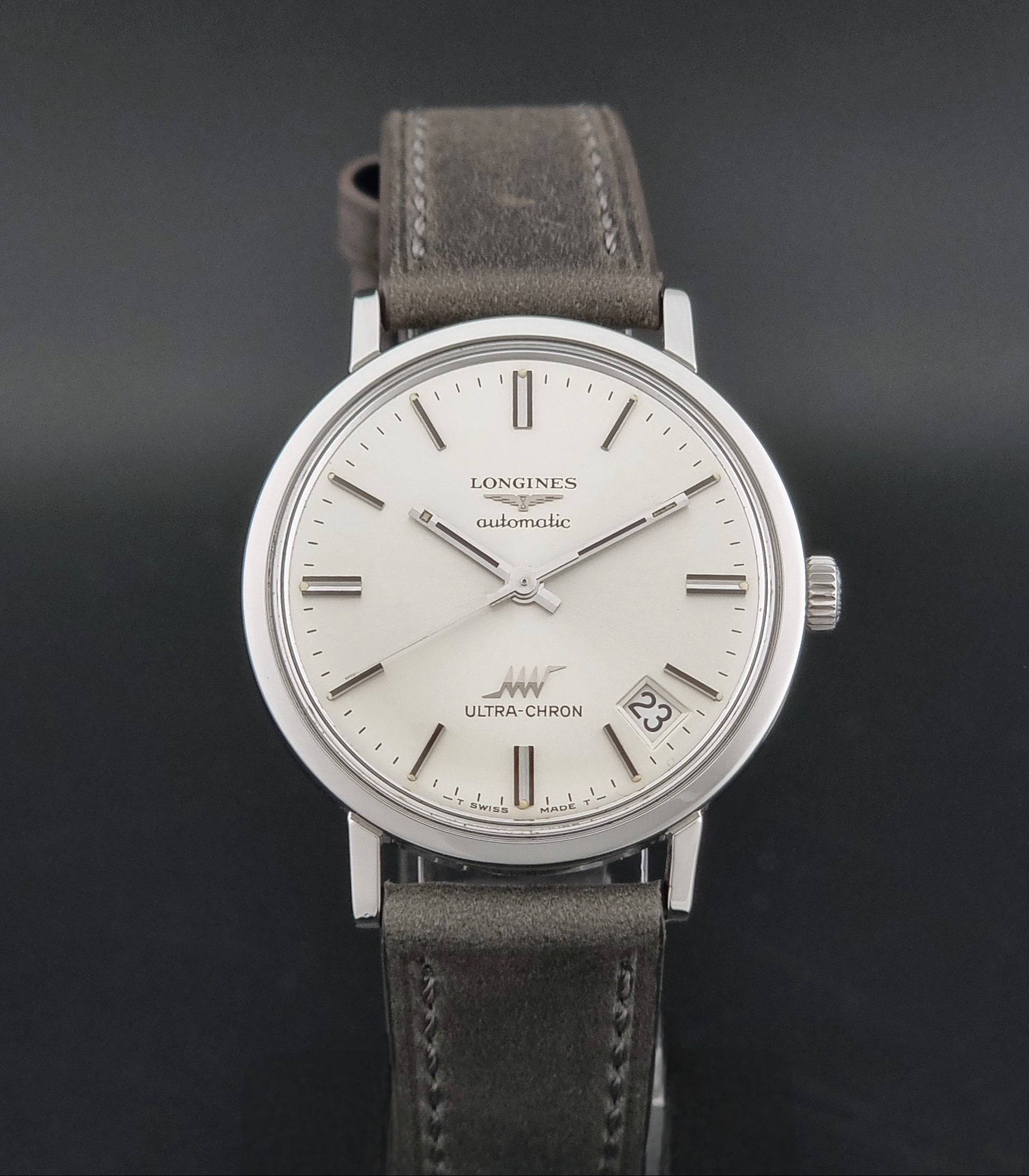 Vintage Longines ULTRA-CHRON 8383-1 watch with a silver-toned round case and gray leather strap on a dark gray background close dial view