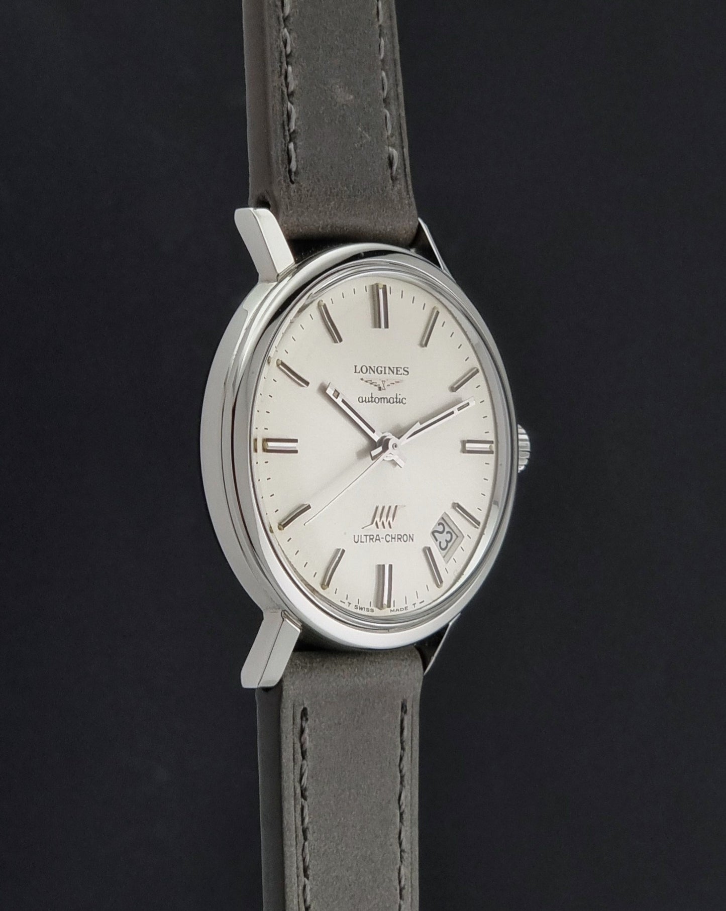 Vintage Longines ULTRA-CHRON 8383-1 watch with a silver-toned round case and gray leather strap on a dark gray background side profiel view