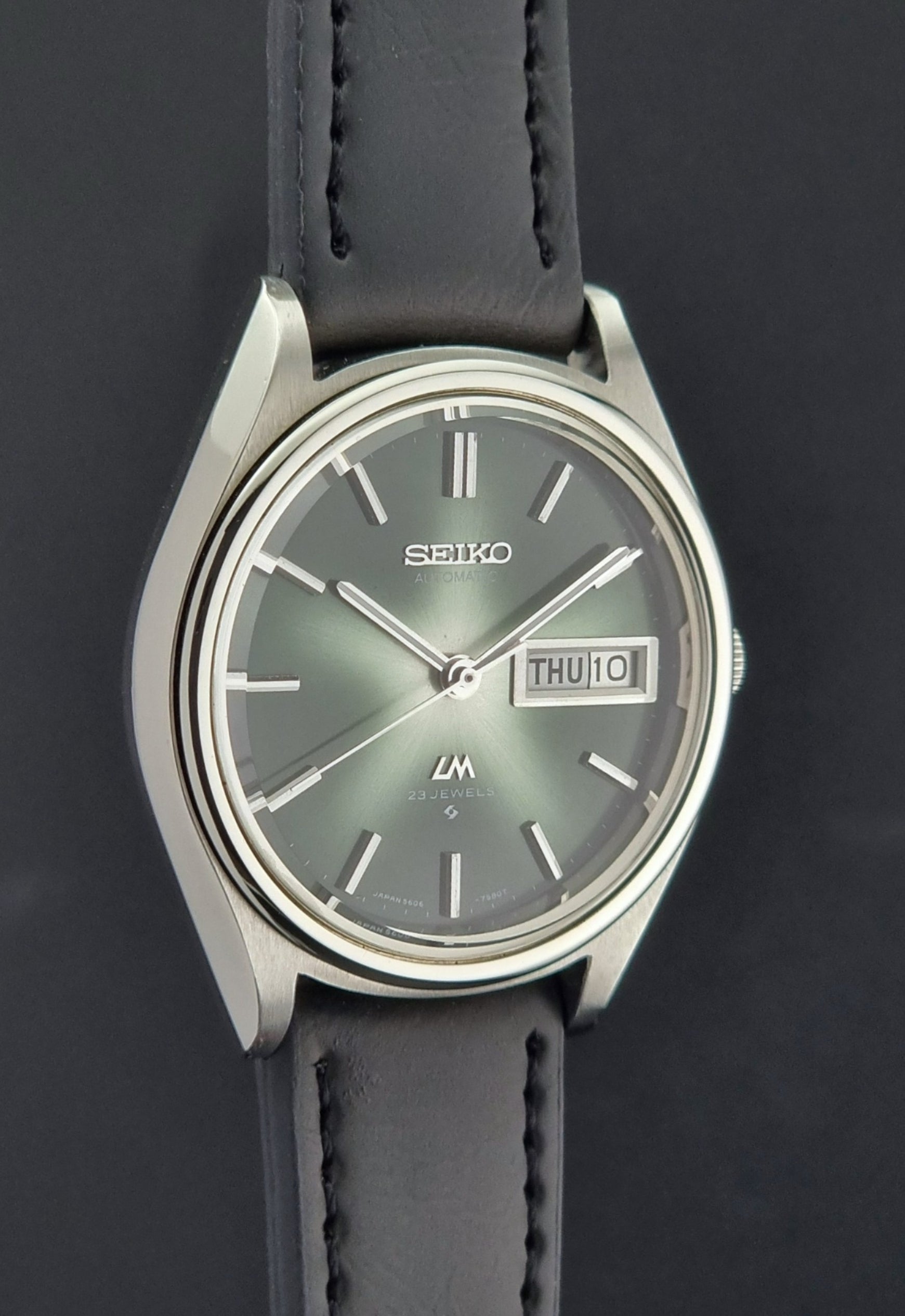 Seiko watch with a dark strap and green dial on a black background