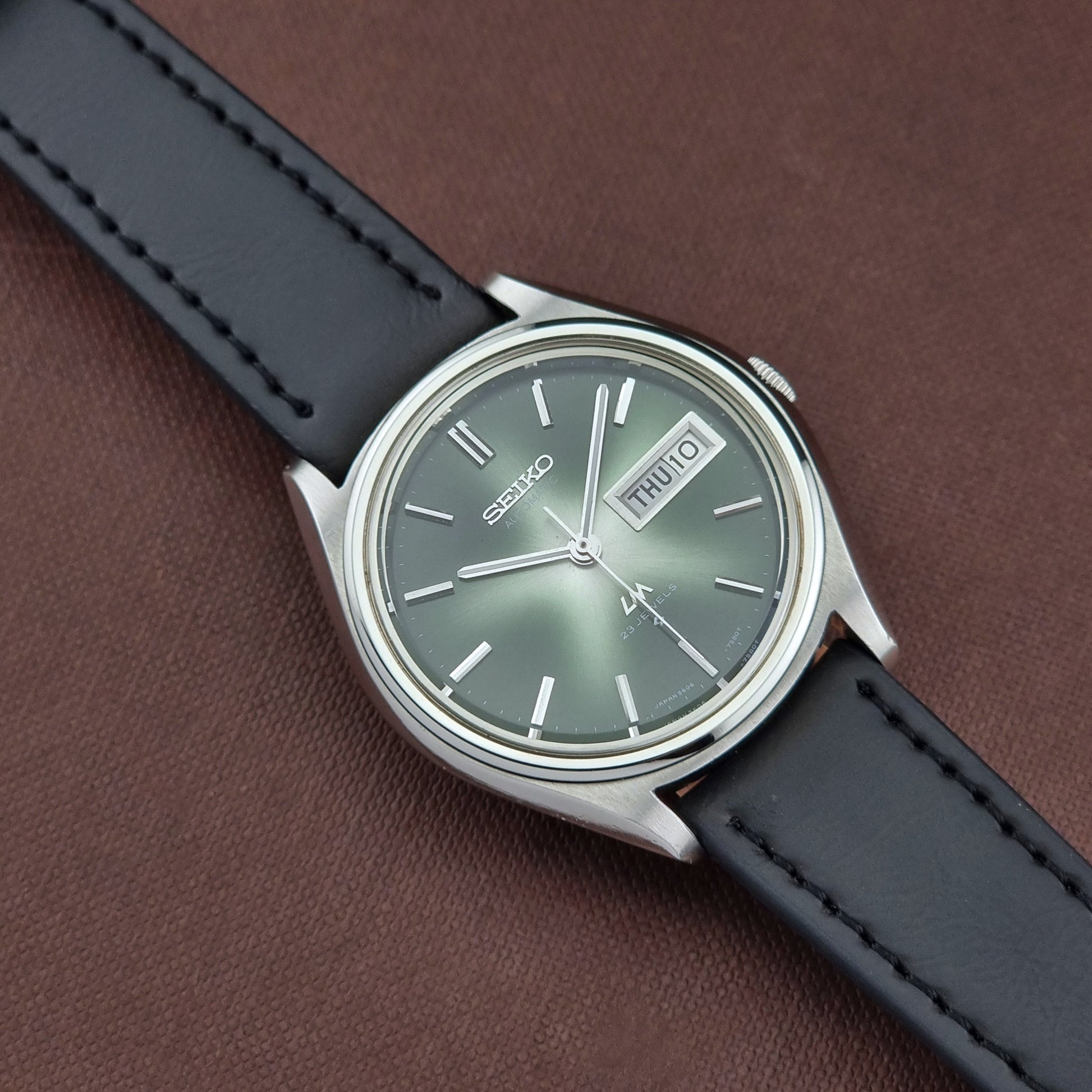 Seiko watch with black leather strap on a brown background