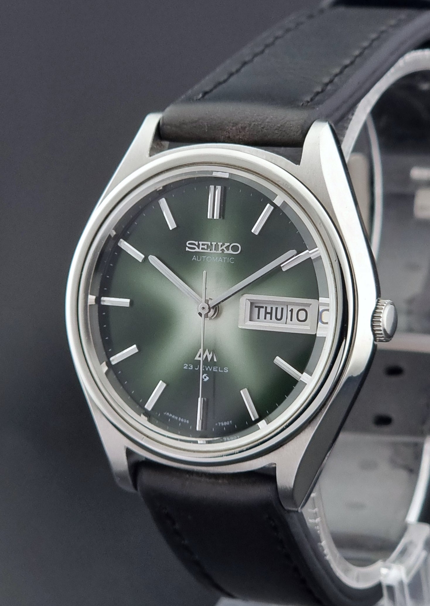 Seiko watch with green face and black leather strap on a dark background