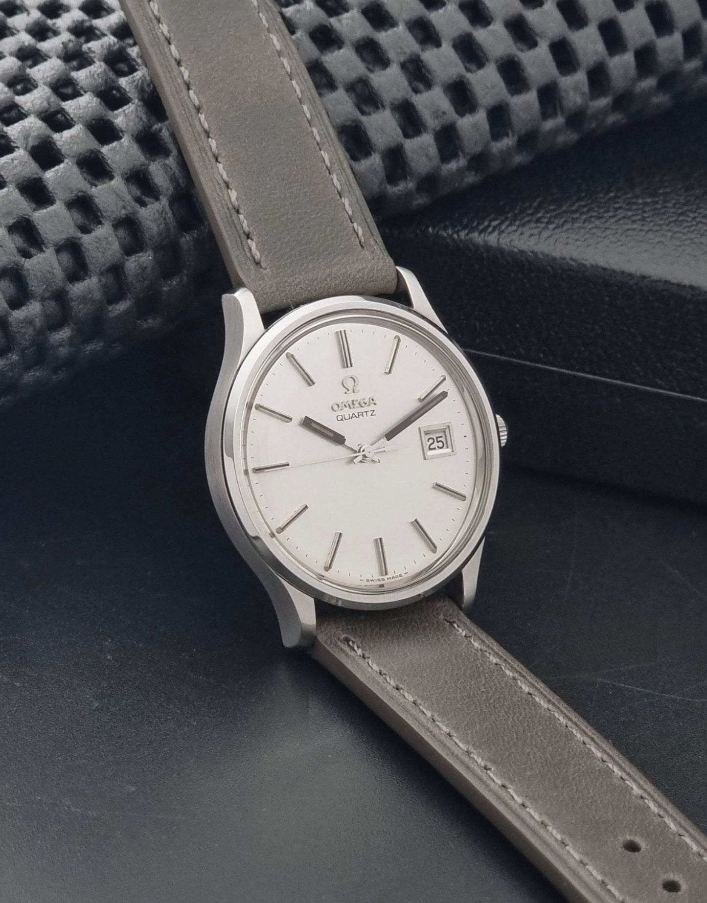Vintage Omega Quartz Wristwatch 196.0071 with a grey strap on a dark background side view