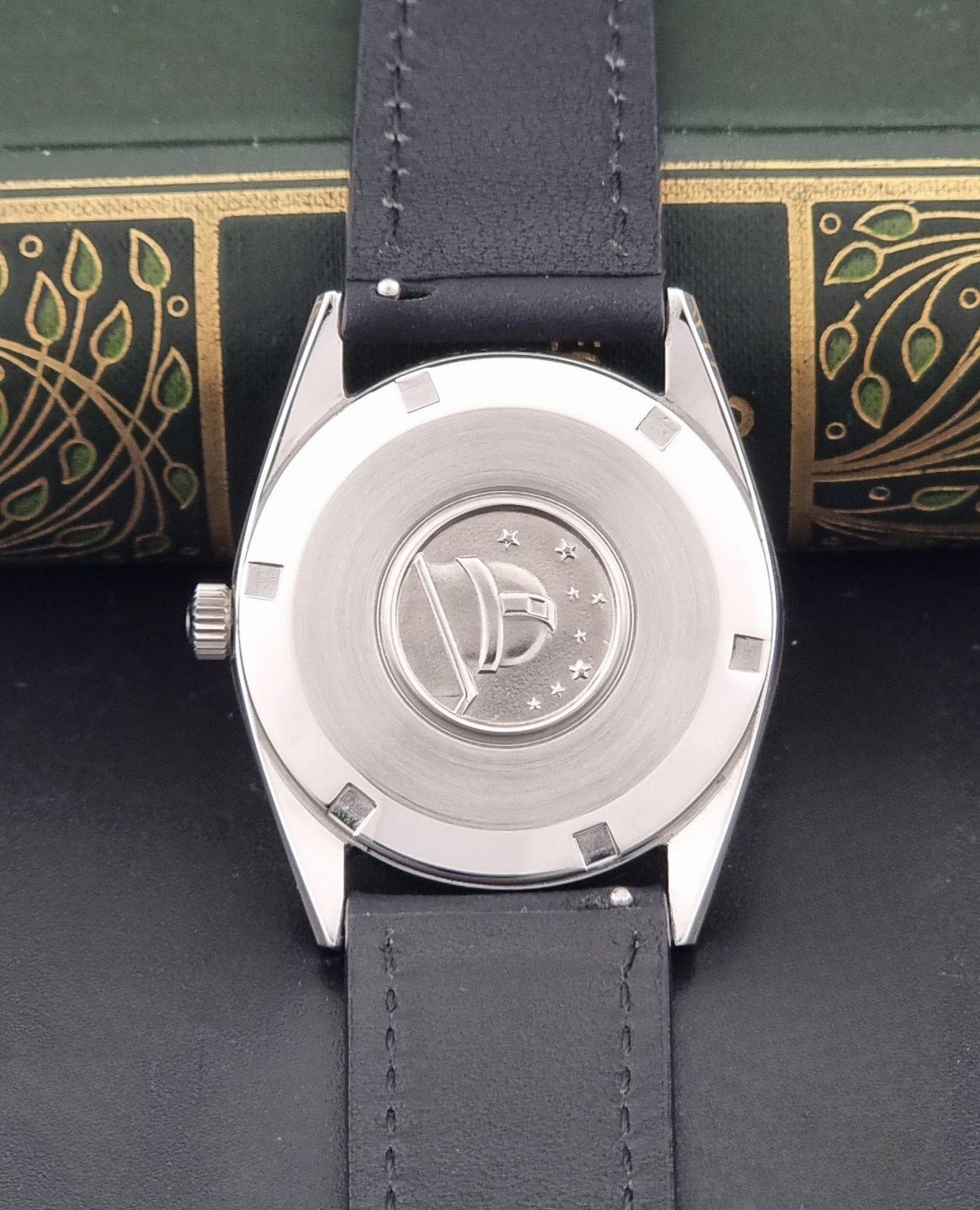 Vintage Omega Constellation 167.021 watch with a silver-toned case and black leather strap, on a dark background case back view