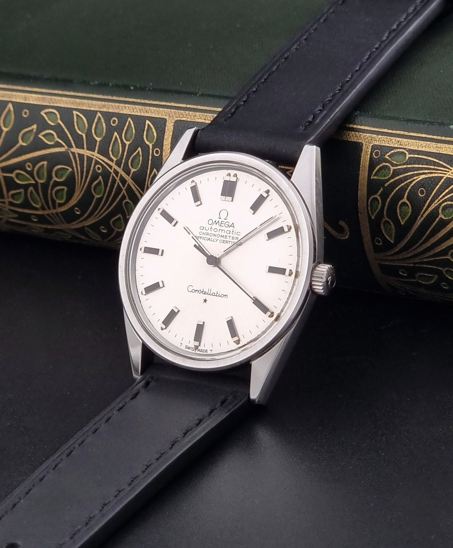 Vintage Omega Constellation 167.021 watch with a silver-toned case and black leather strap, on a dark background crown view
