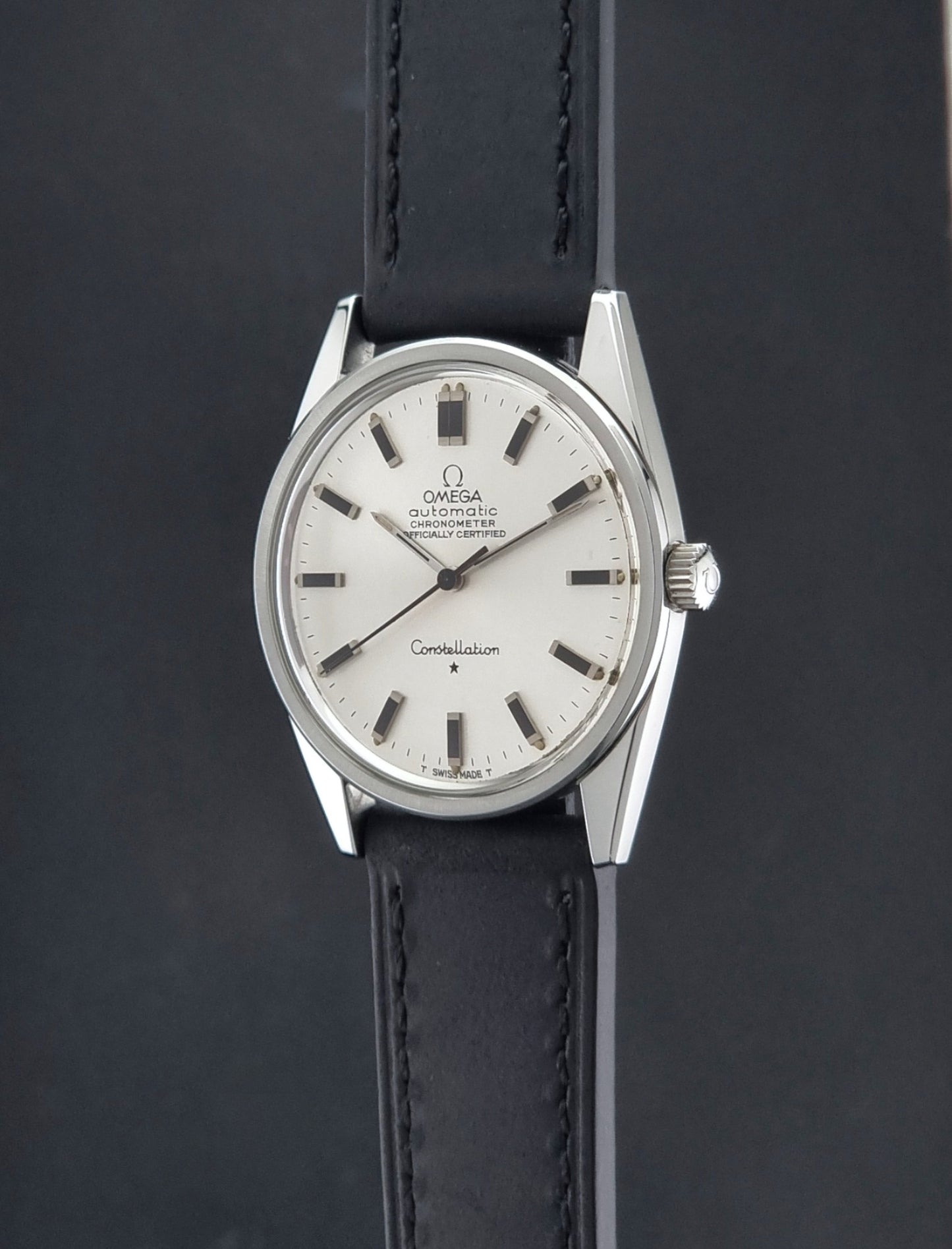 Vintage Omega Constellation 167.021 watch with a silver-toned case and black leather strap, on a dark background crown profile view