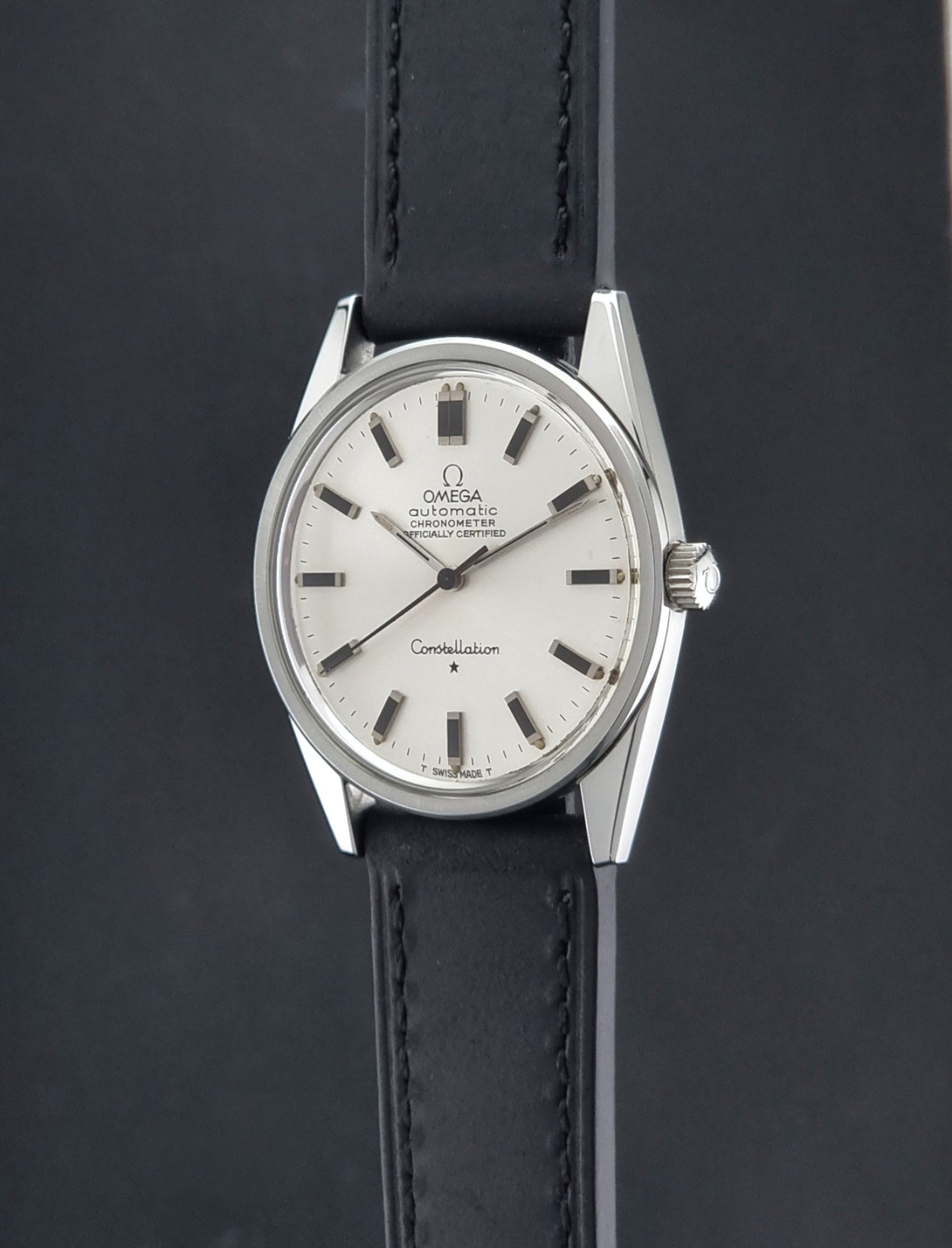 Vintage Omega Constellation 167.021 watch with a silver-toned case and black leather strap, on a dark background crown profile view