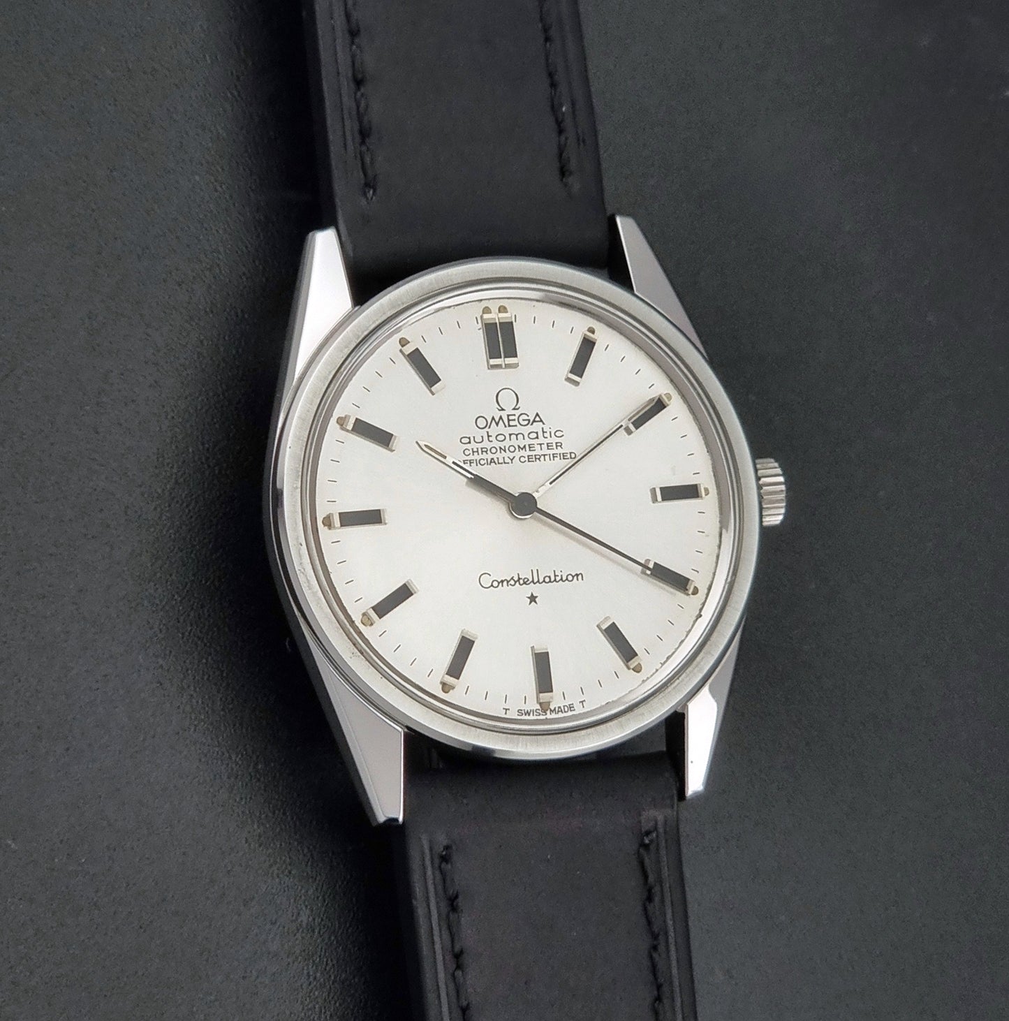 Vintage Omega Constellation 167.021 watch with a silver-toned case and black leather strap, on a dark background front view