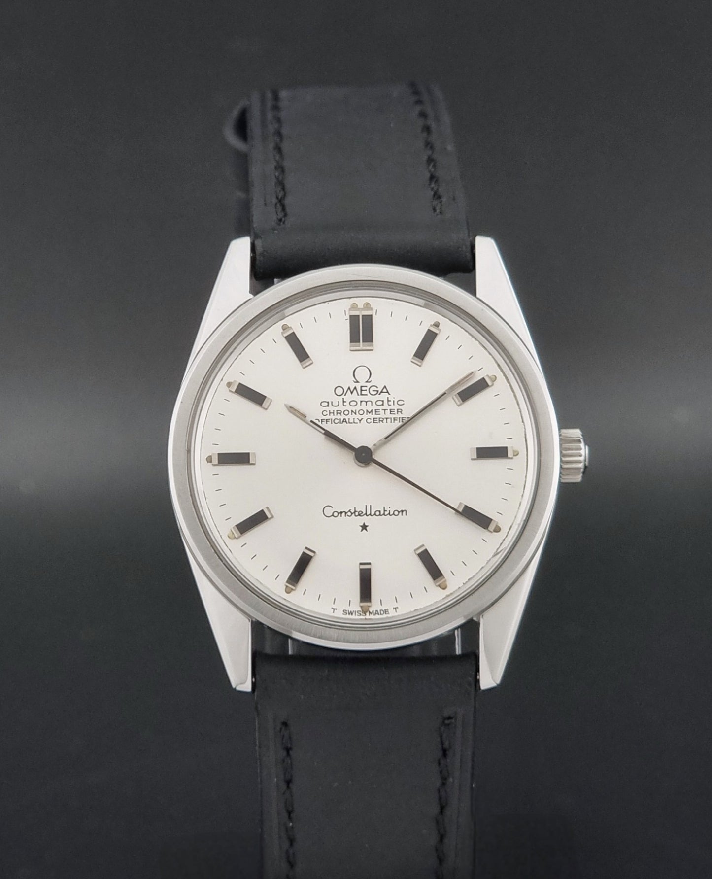 Vintage Omega Constellation 167.021 watch with a silver-toned case and black leather strap, on a dark background close dial view