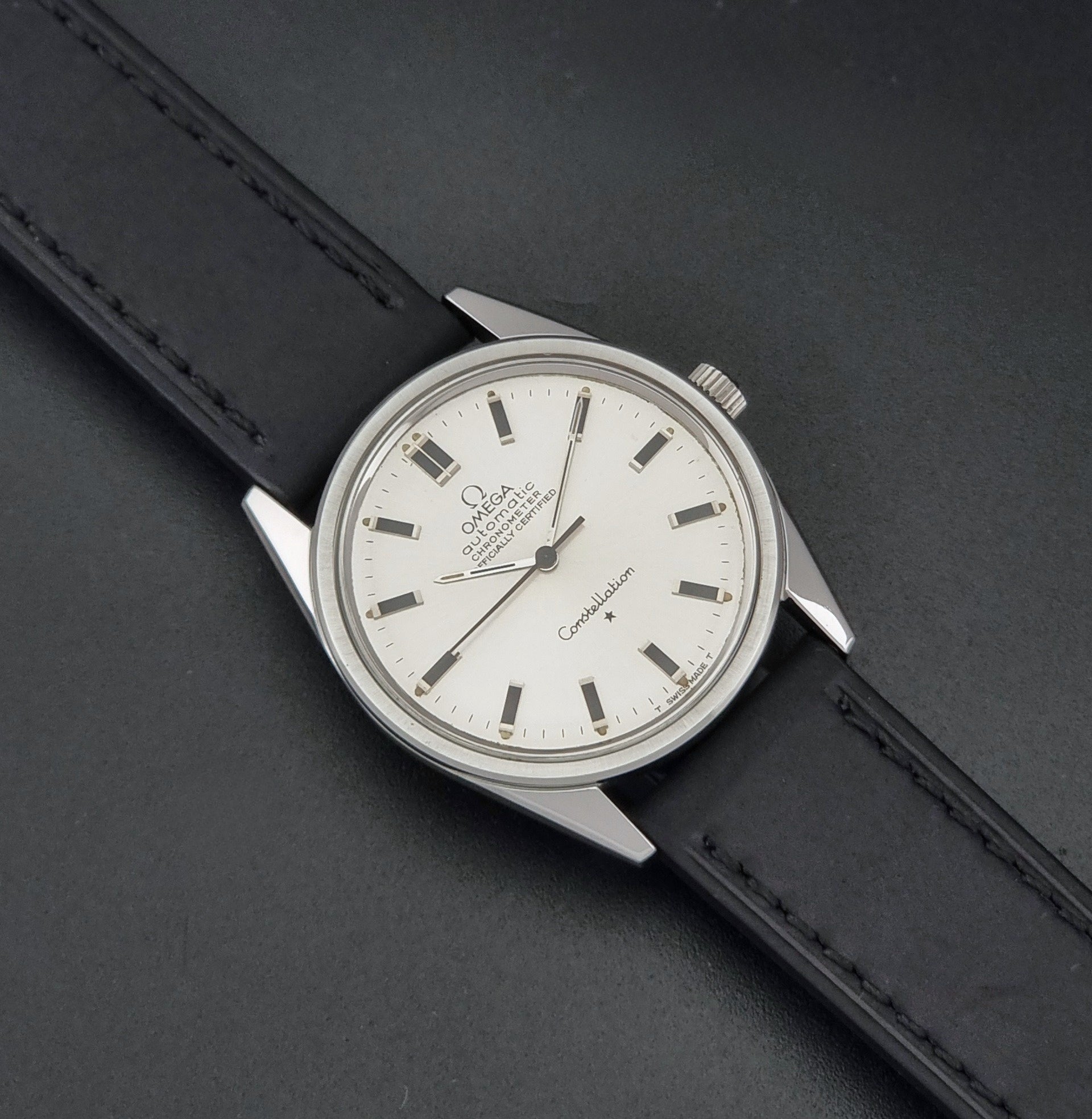 Vintage Omega Constellation 167.021 watch with a silver-toned case and black leather strap, on a dark background dial