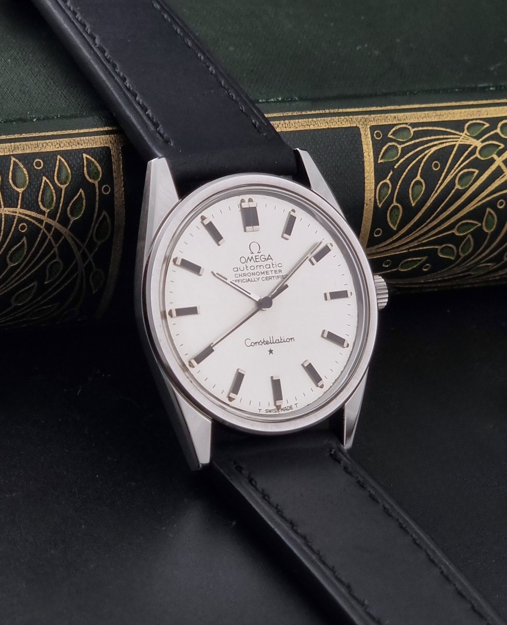 Vintage Omega Constellation 167.021 watch with a silver-toned case and black leather strap, on a dark background side view