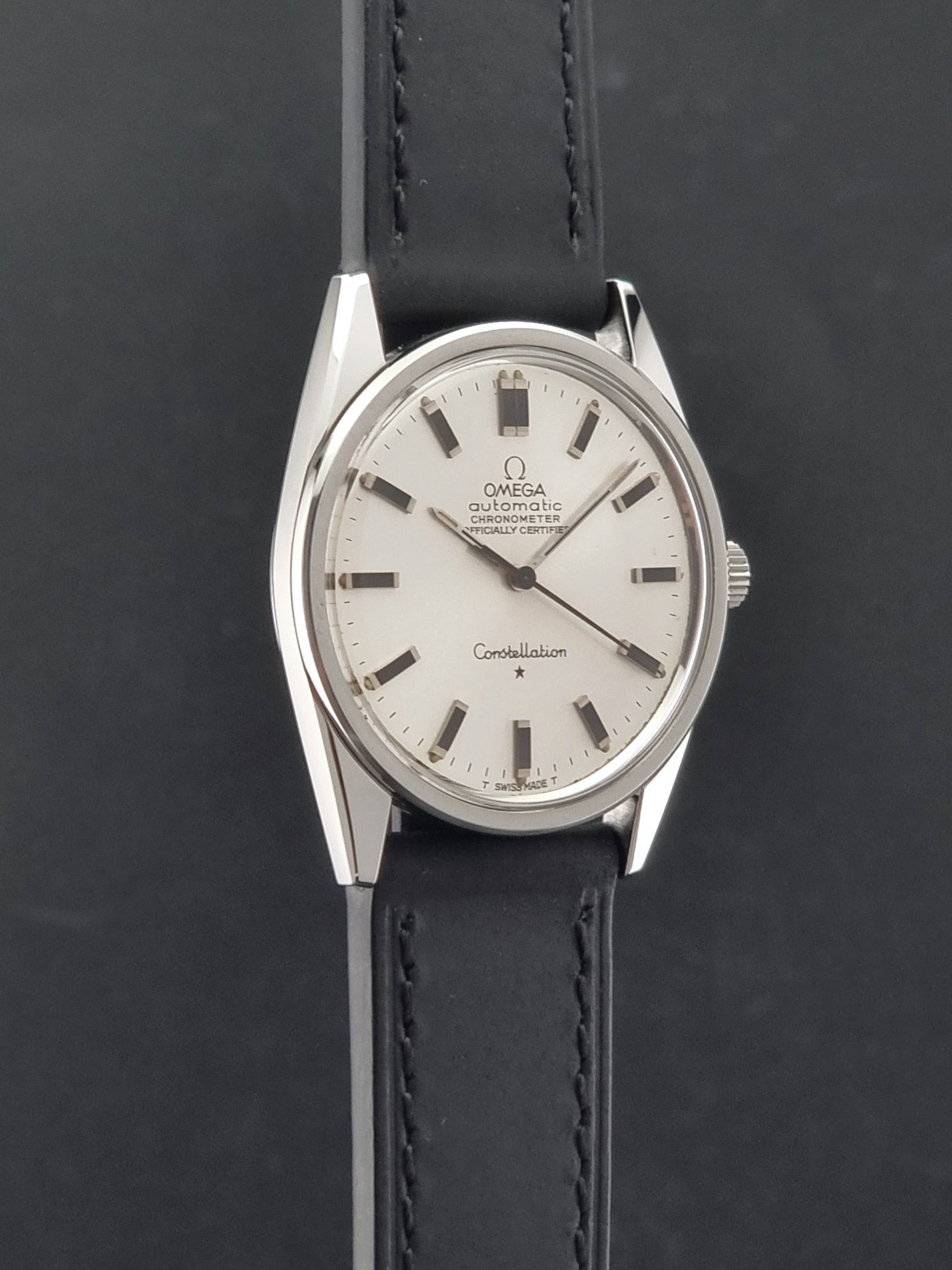 Vintage Omega Constellation 167.021 watch with a silver-toned case and black leather strap, on a dark background side profile view