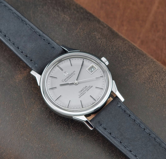 Omega watch with a silver dial and black leather strap on a brown textured surface