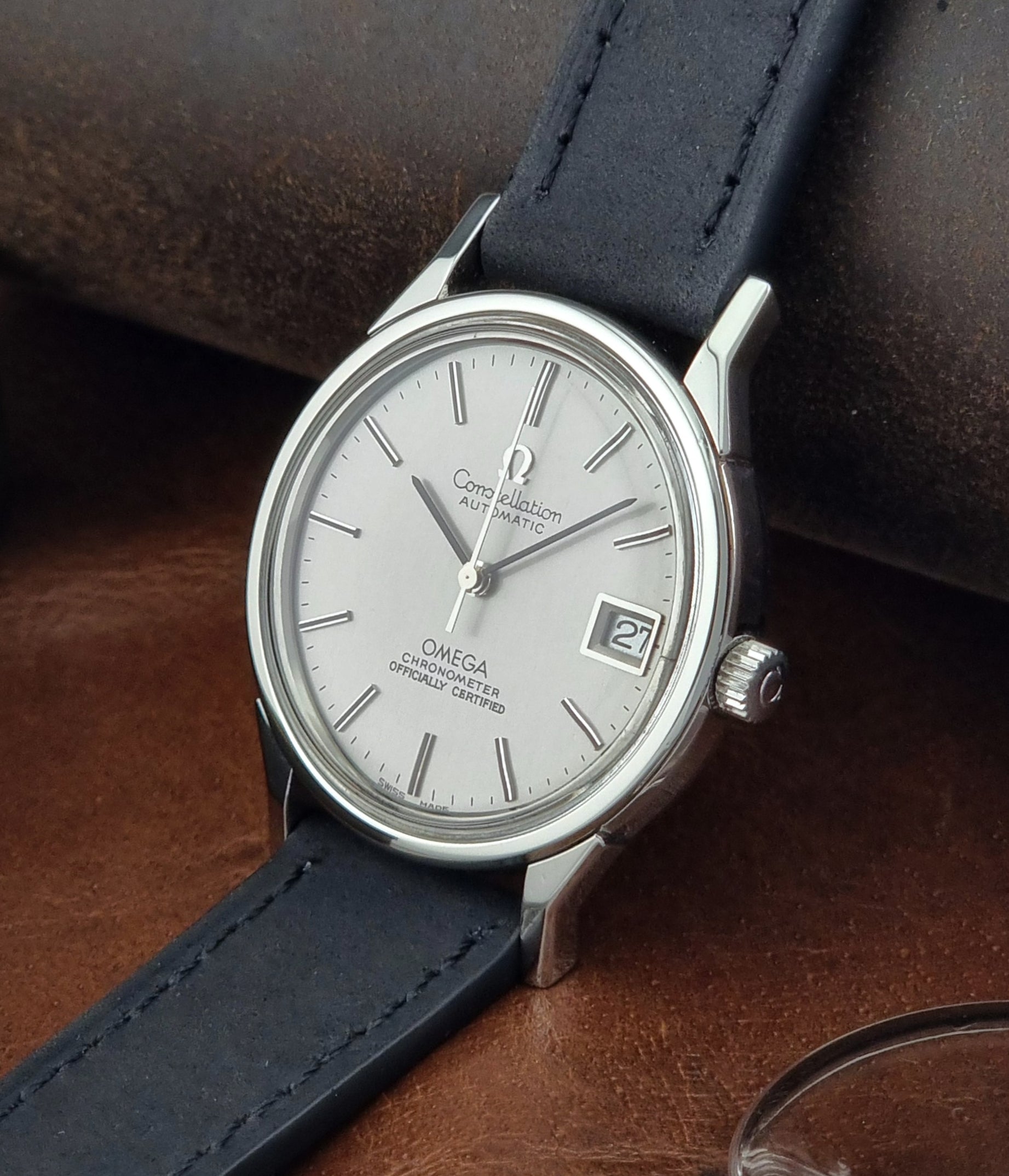 Omega watch with a silver dial and black leather strap on a brown surface