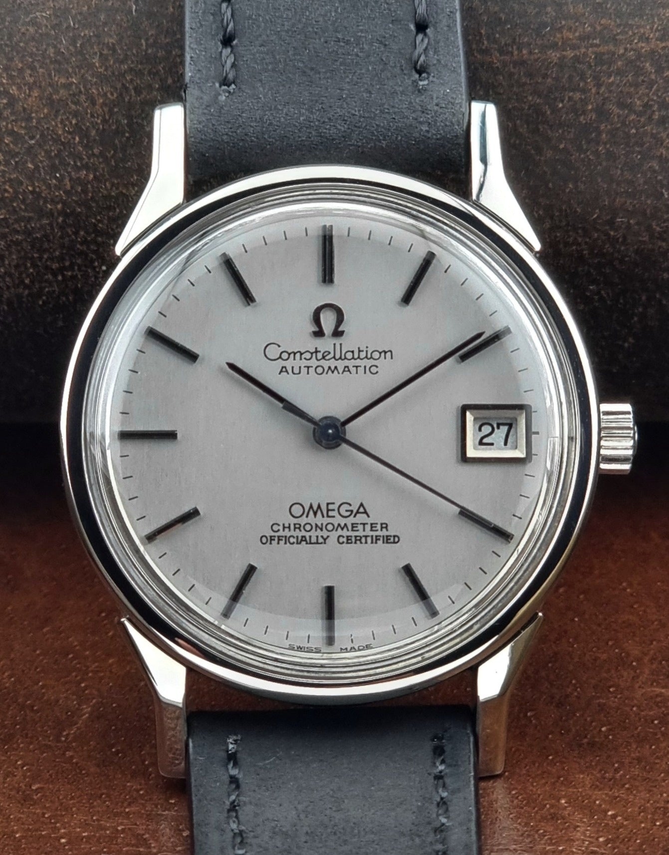 Omega watch with silver case and black leather strap on a brown background